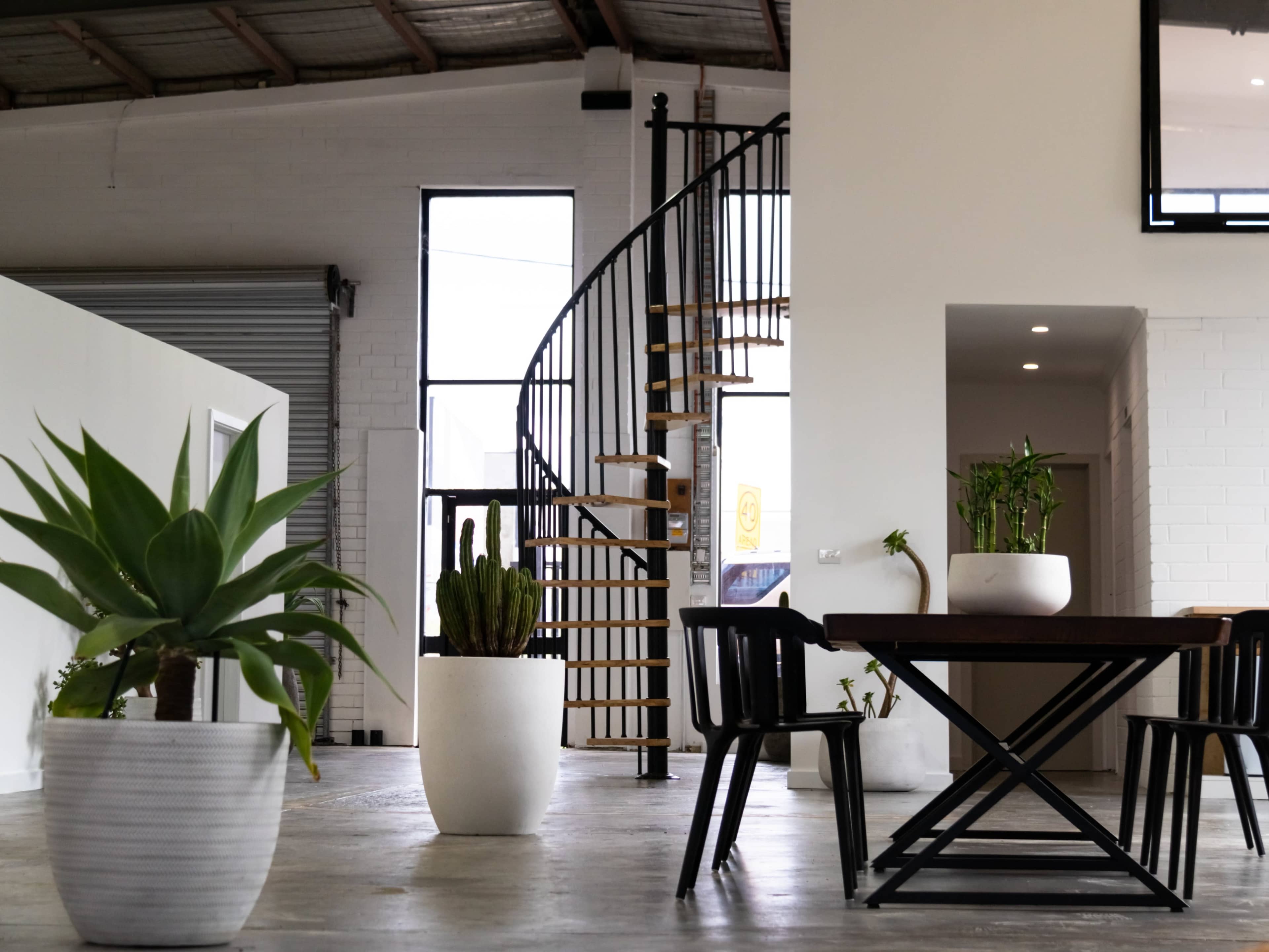 A modern interior space featuring a spiral staircase, a wooden table with black chairs, and several potted plants.