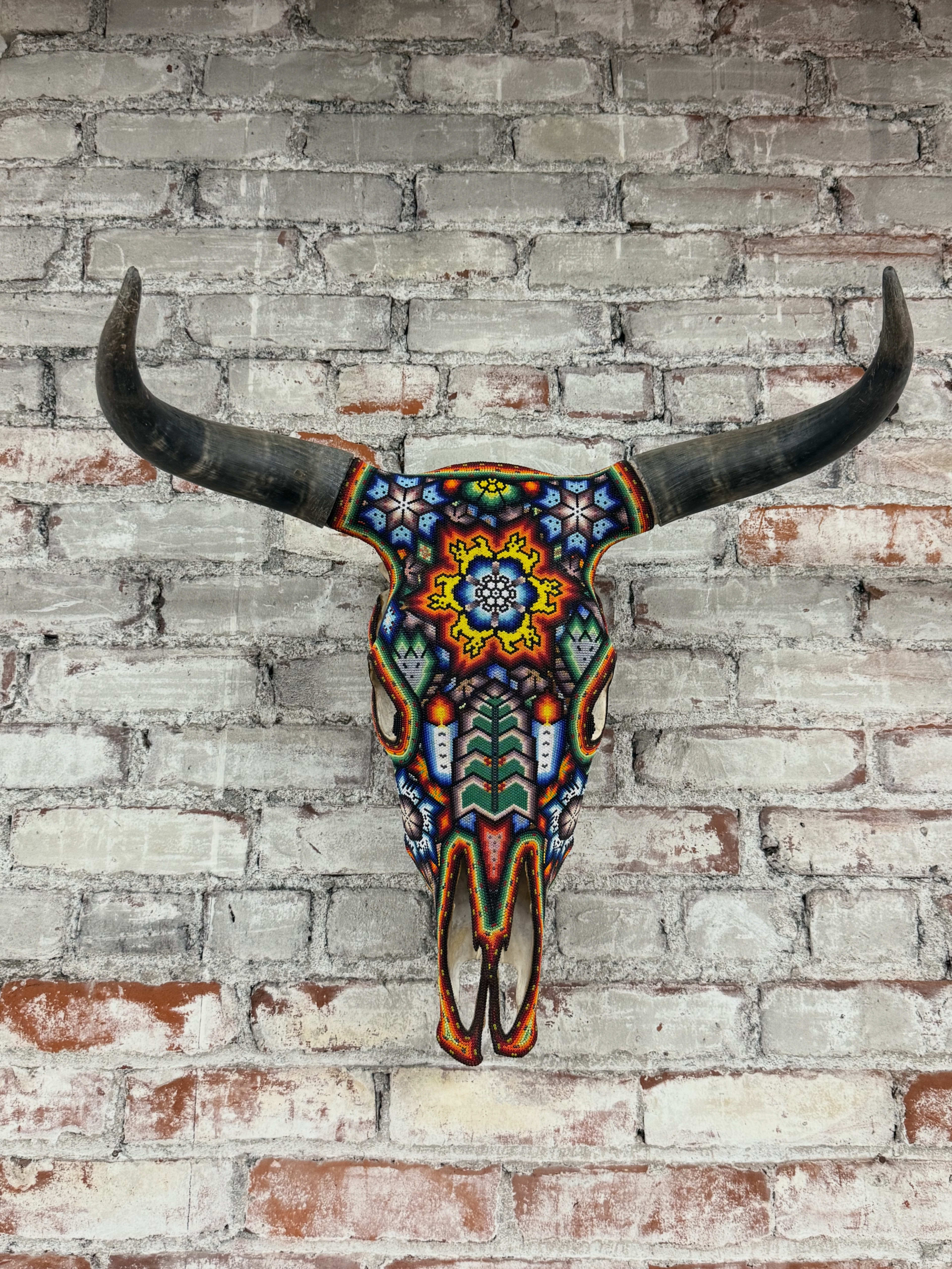 A brightly painted bull skull is mounted on a brick wall.