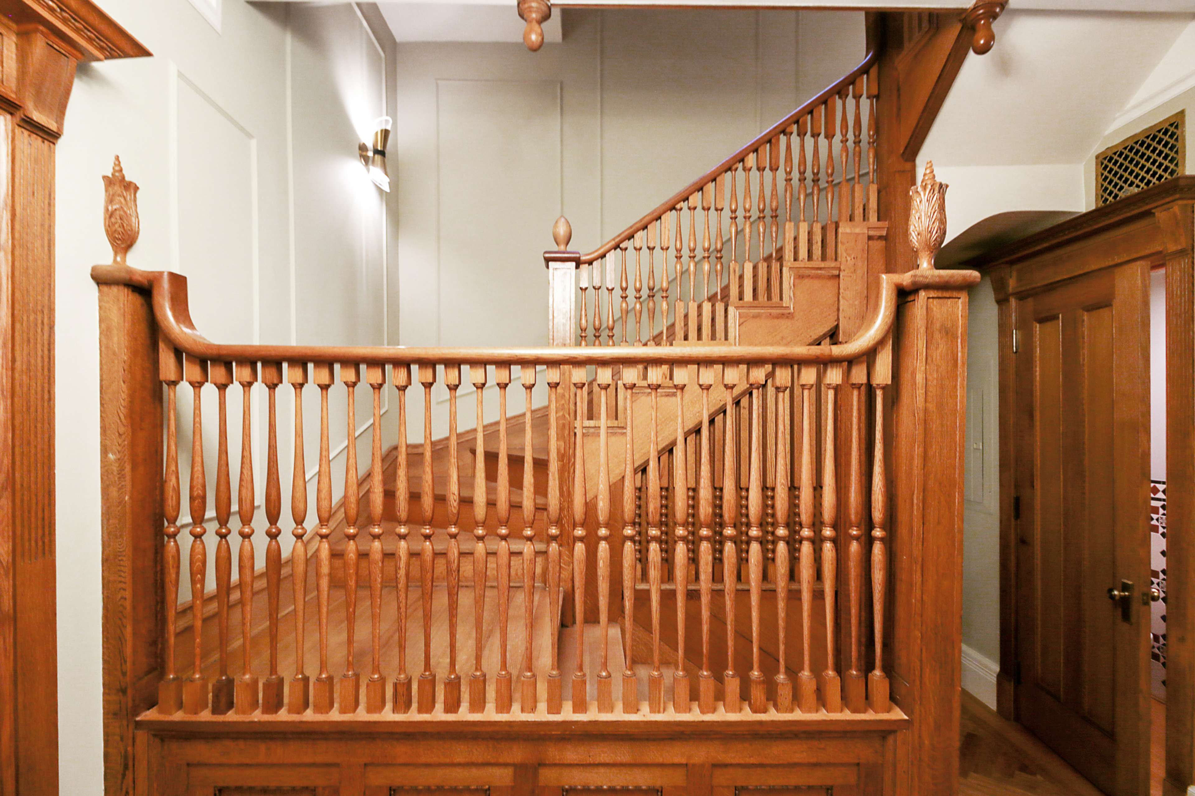 A wooden staircase with ornate railings and a landing at the top, situated in a well-lit hallway.