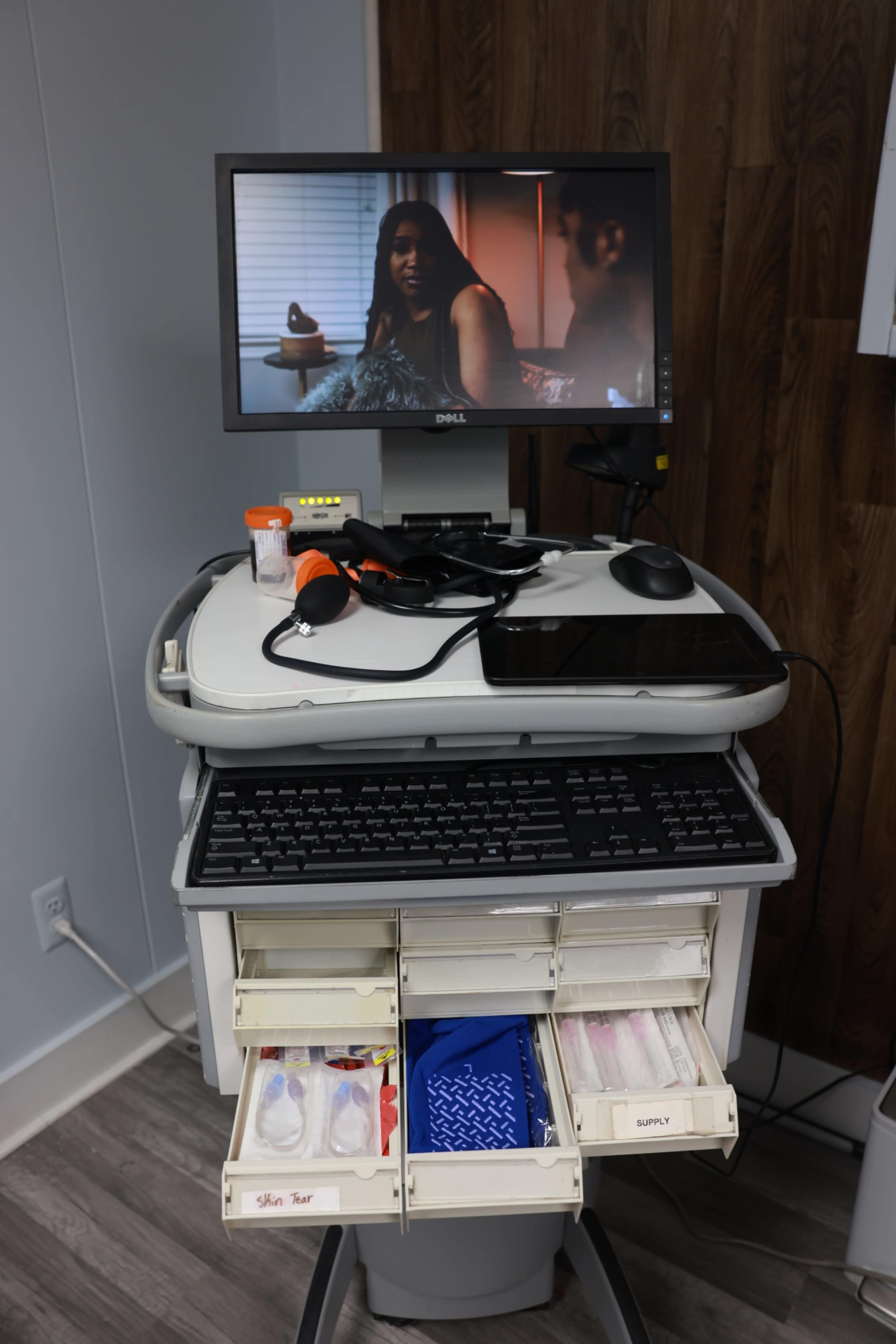 A medical cart with a computer monitor displaying a scene from a movie, equipped with drawers containing medical supplies.