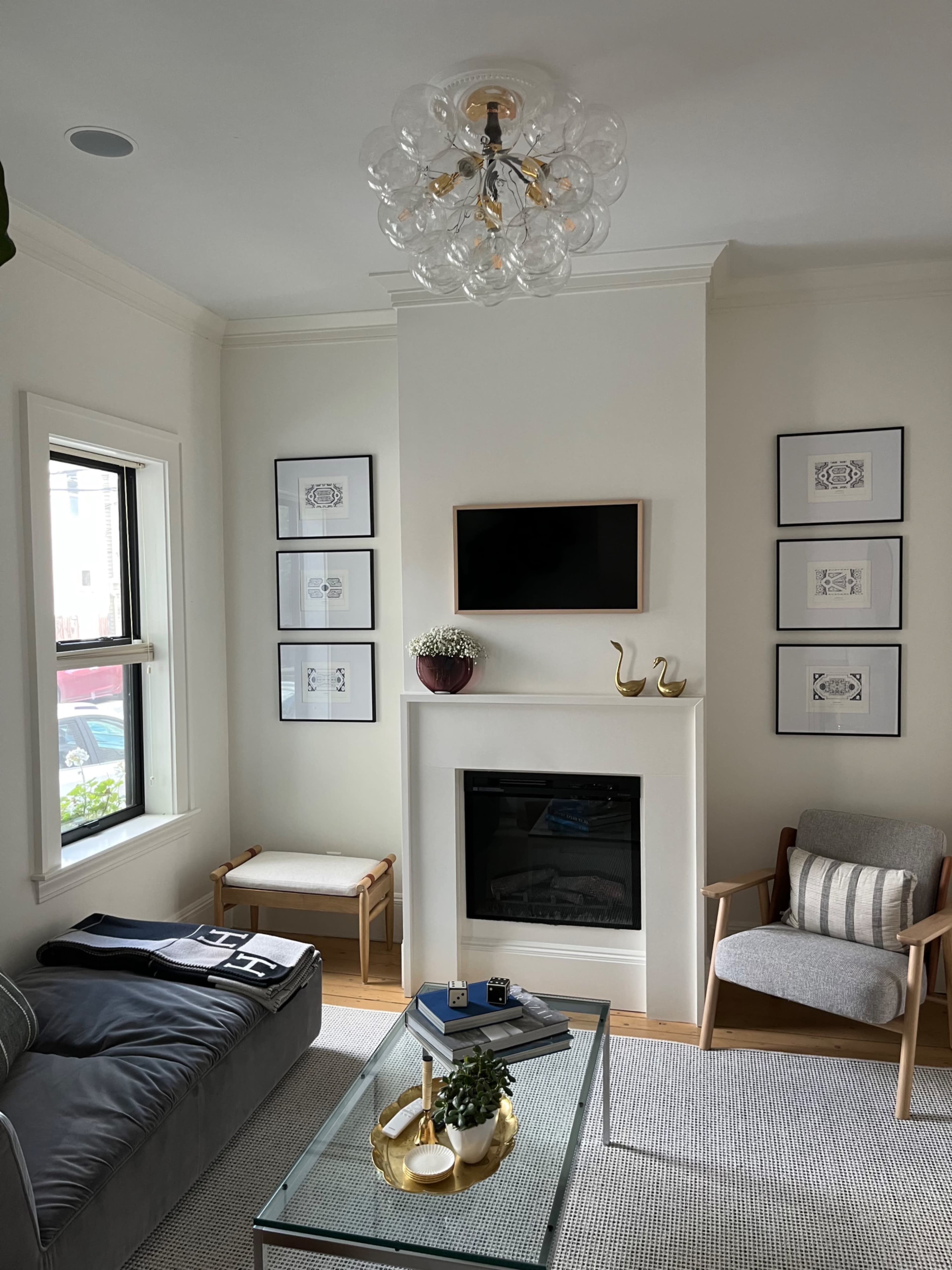 A modern living room with a gray sofa, a glass coffee table, a fireplace, and framed artwork on the walls.