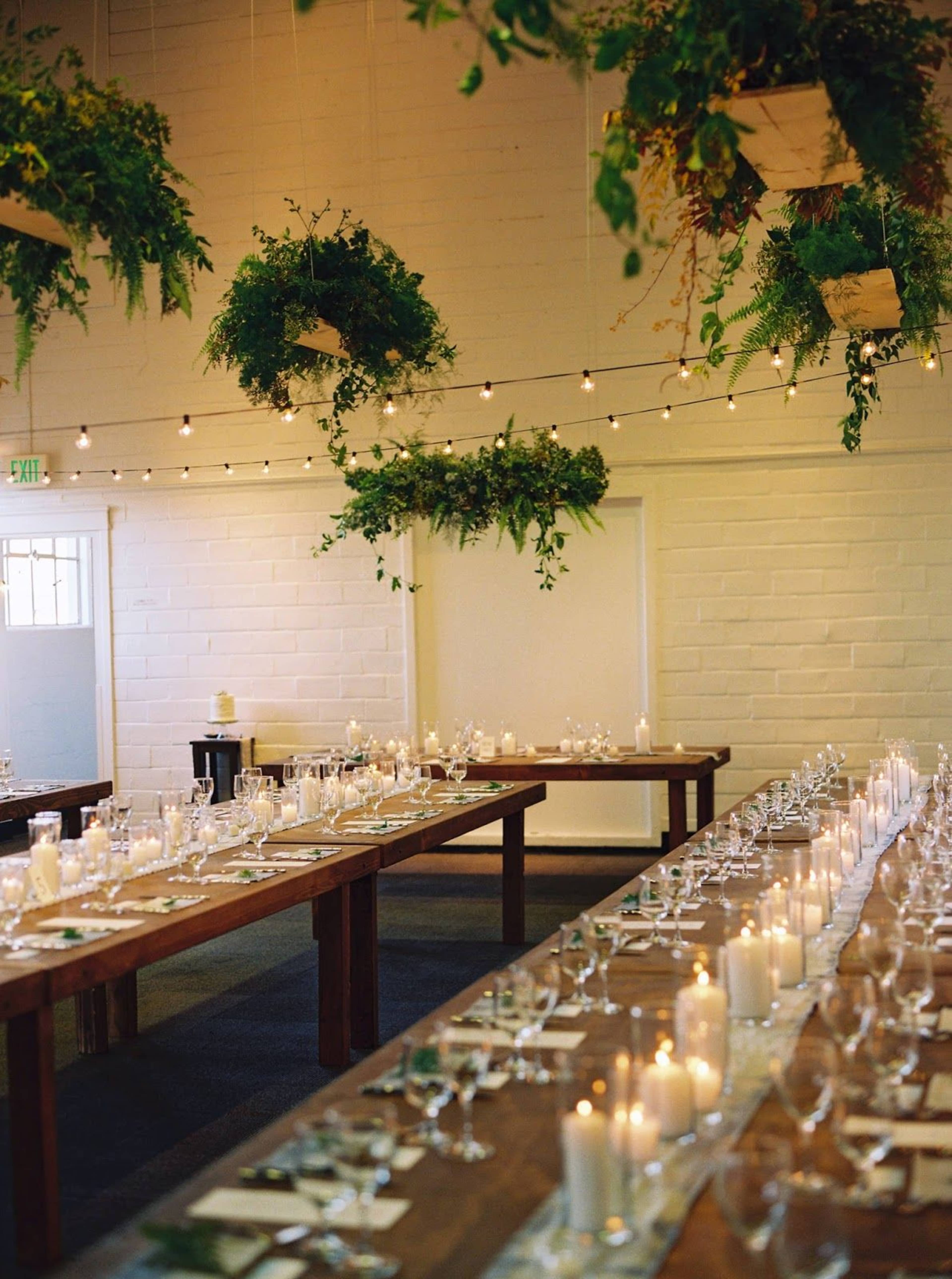 A spacious dining area decorated with hanging greenery, candlelit tables, and arranged glassware, creating a festive atmosphere.