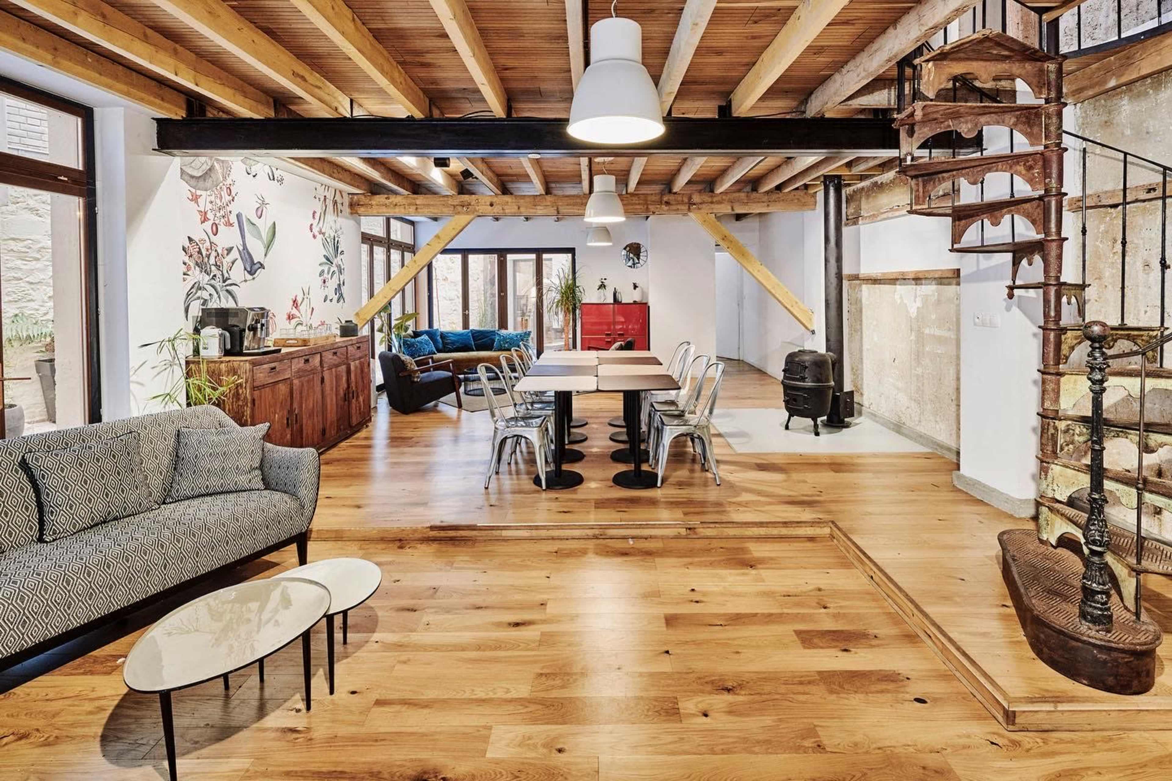The scene features a spacious living area with wooden beams, a mix of modern and rustic furniture, and a spiral staircase leading to an upper level.
