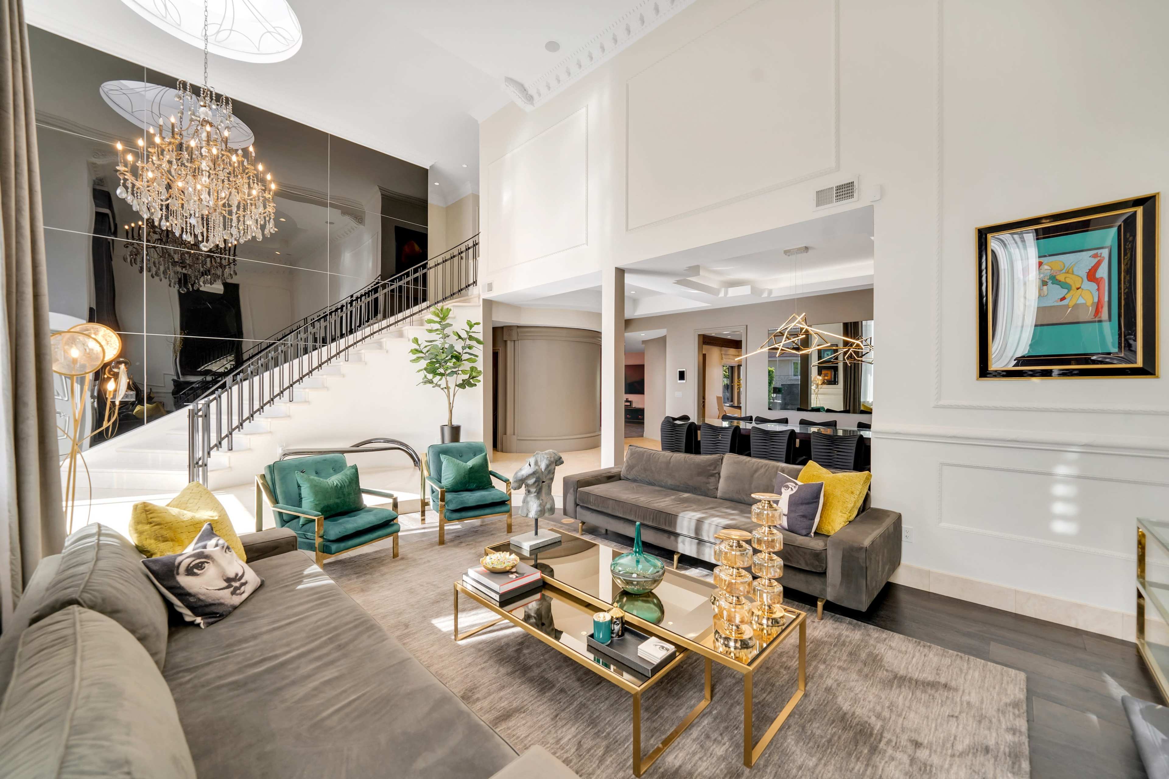 A modern living room with a curved staircase, elegant furnishings, and a chandelier above.