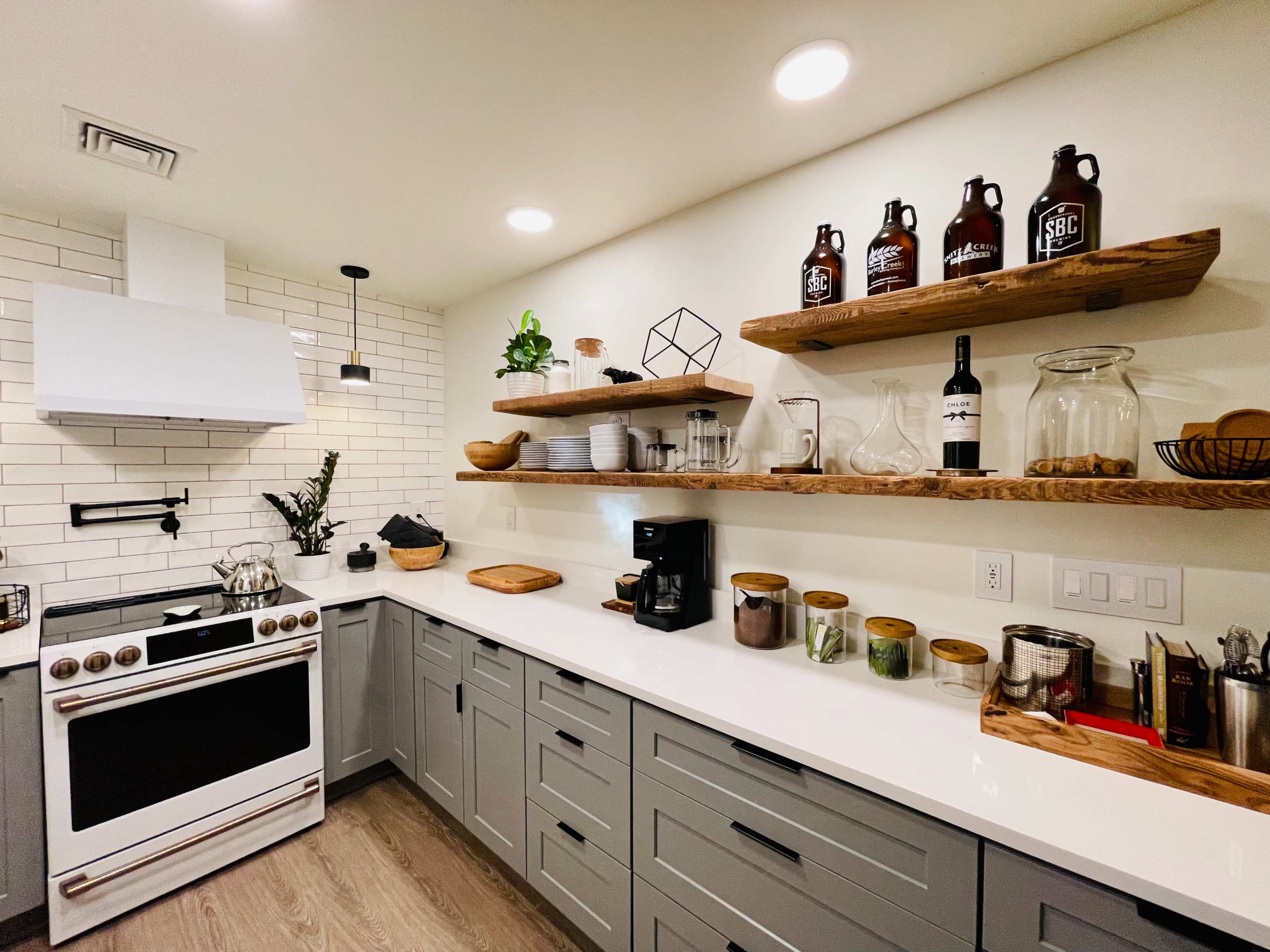 A modern kitchen features a white stove, open wooden shelves with various kitchen items, and a clean countertop with a coffee maker and decorative plants.