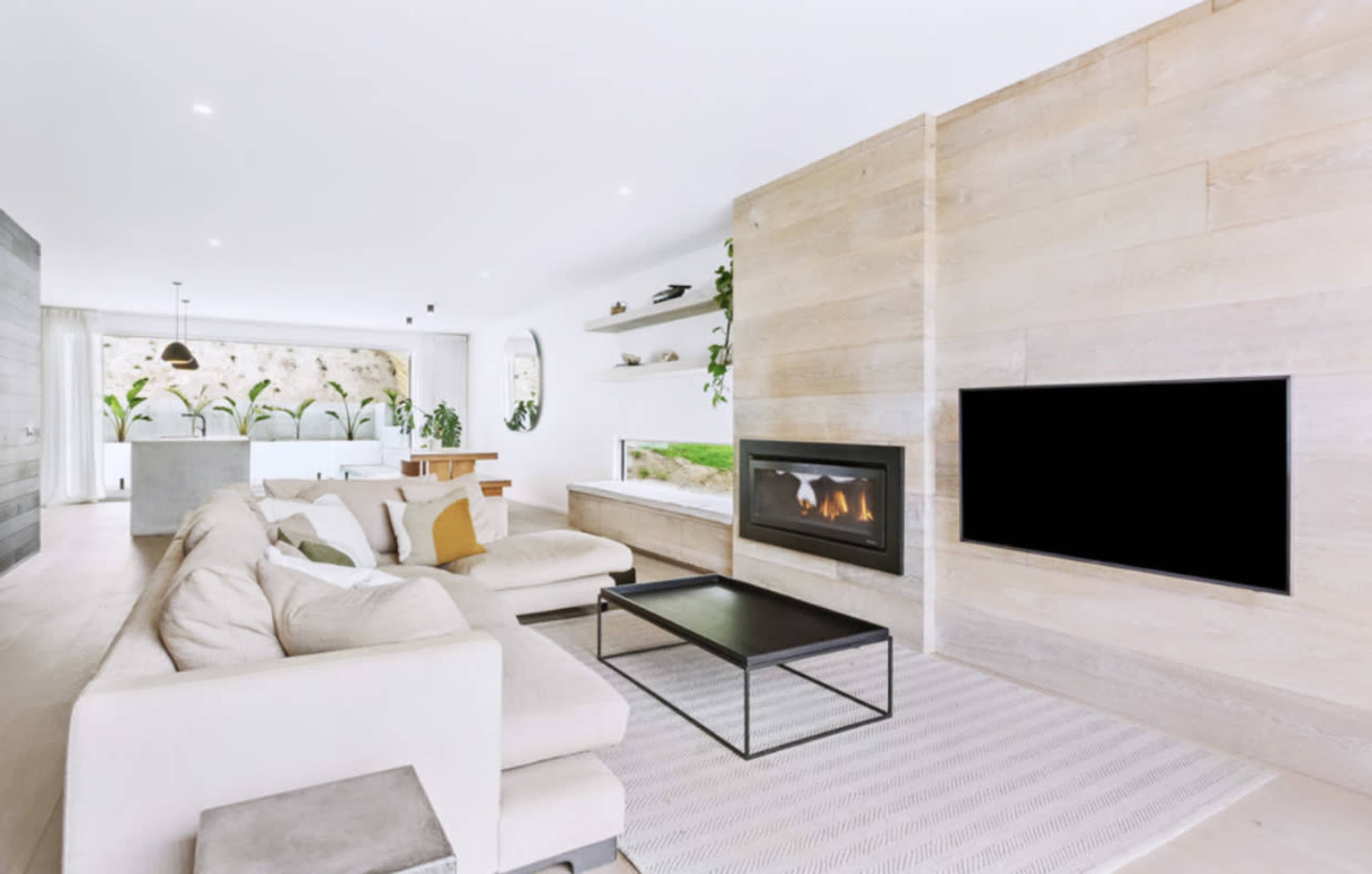 A modern living room features a sectional sofa, a coffee table, and a fireplace integrated into a wooden panel wall.