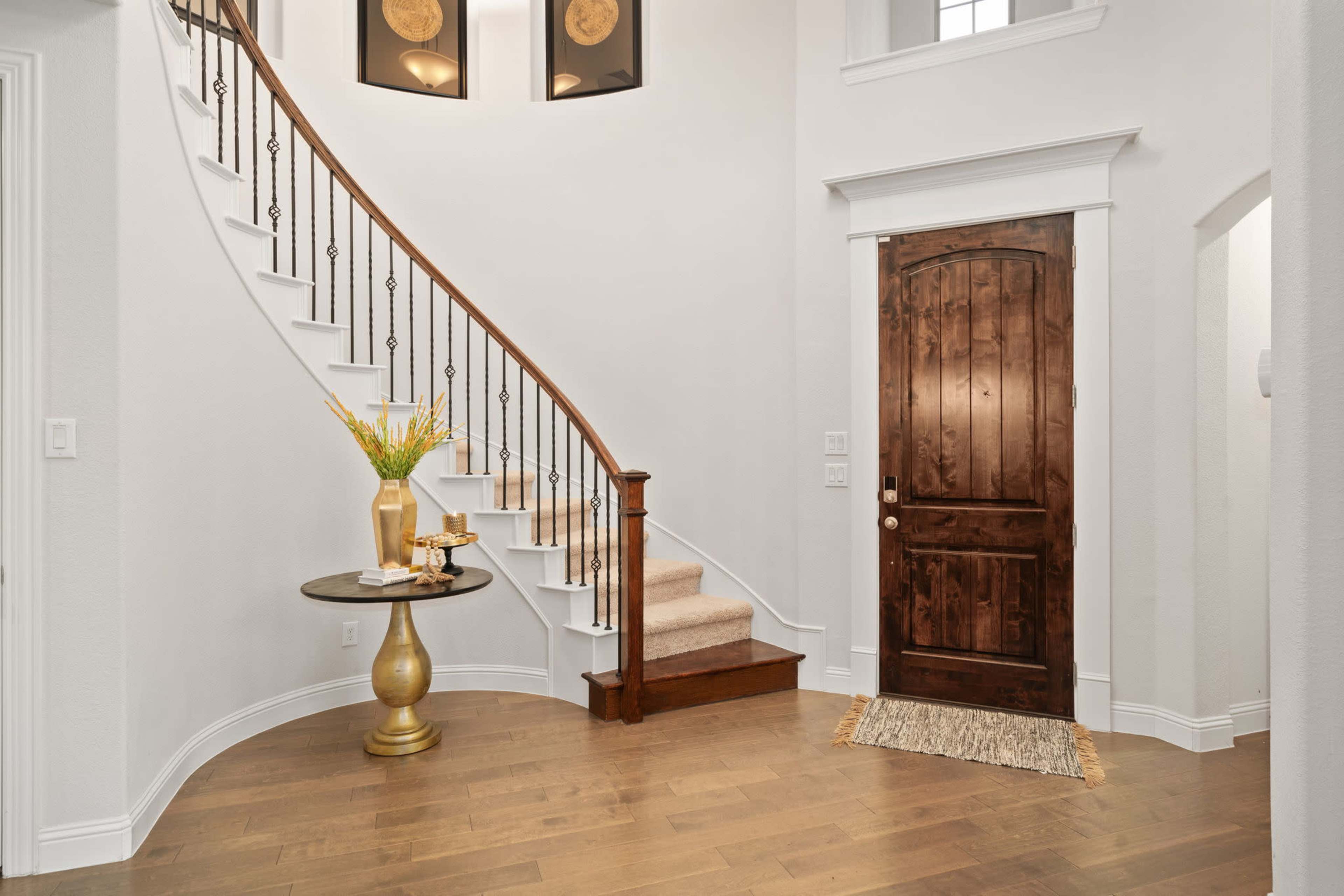 A spacious foyer with a curved staircase, a wooden front door, and a decorative table topped with a vase.