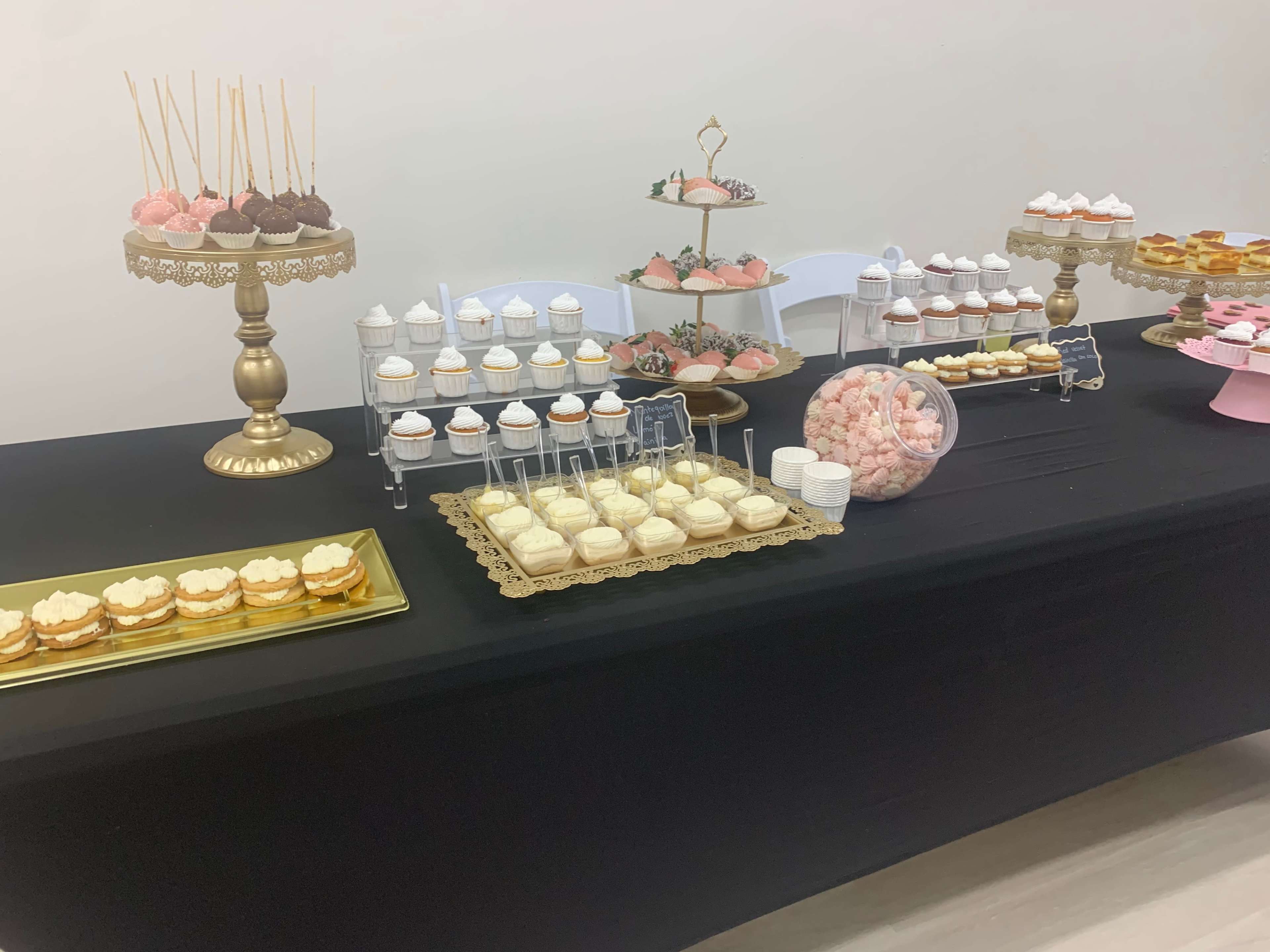 A dessert table features an array of cupcakes, pastries, and candies displayed on various stands and trays.