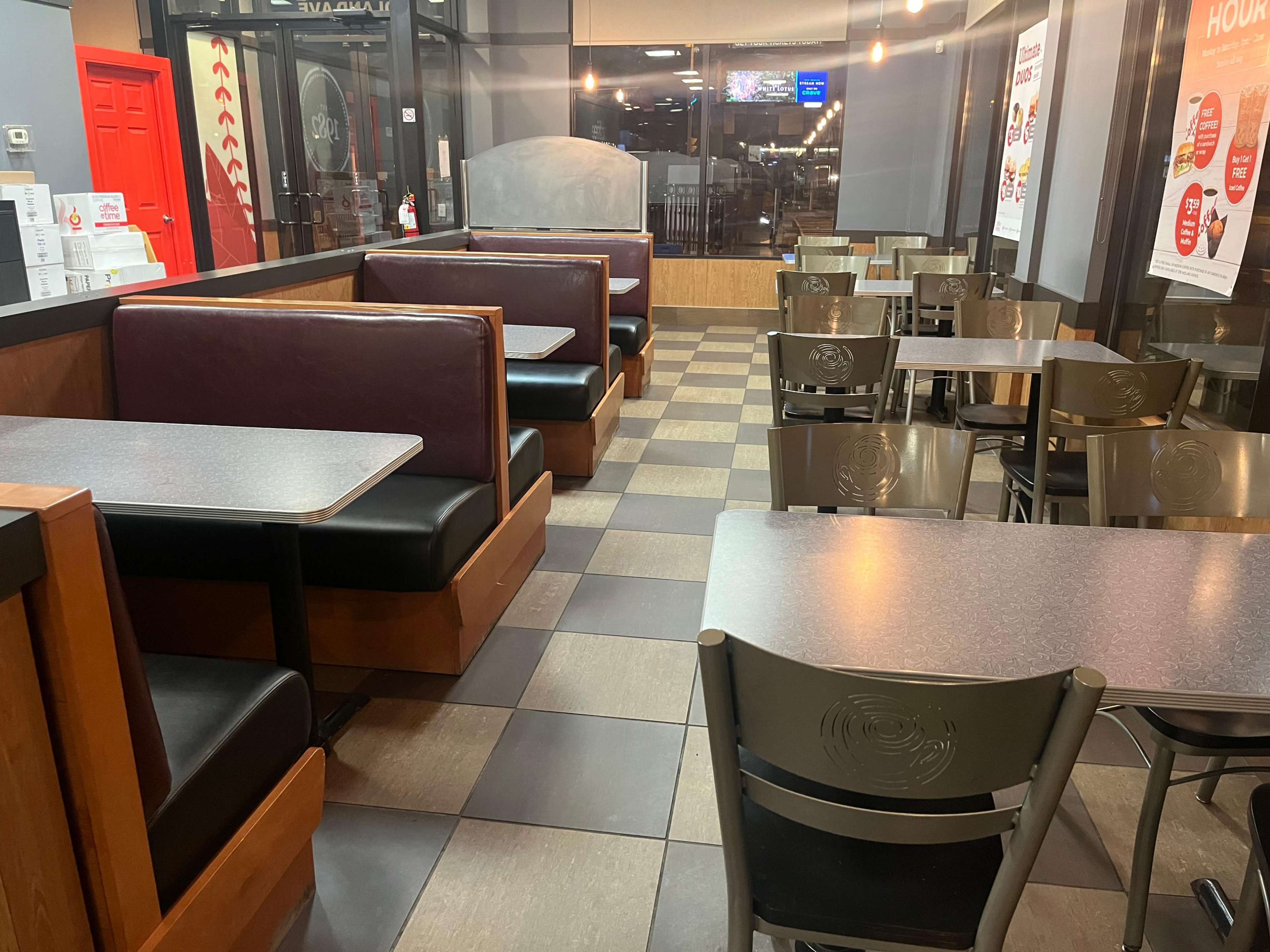 The image shows a fast-food restaurant interior with empty booths and tables arranged on a tiled floor.