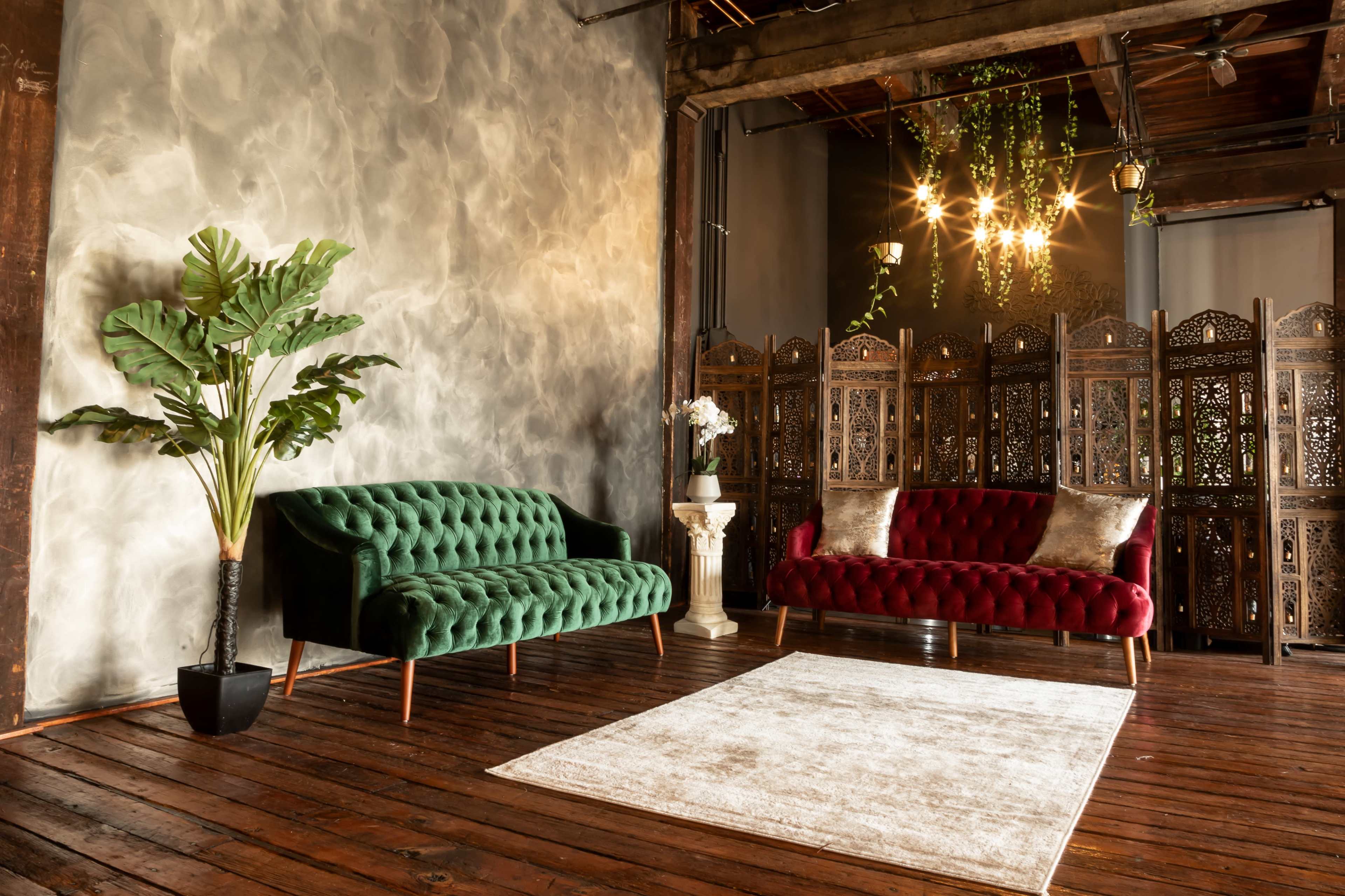A stylish interior with a green sofa, a red sofa, a decorative screen, a potted plant, and a central area rug on a wooden floor.