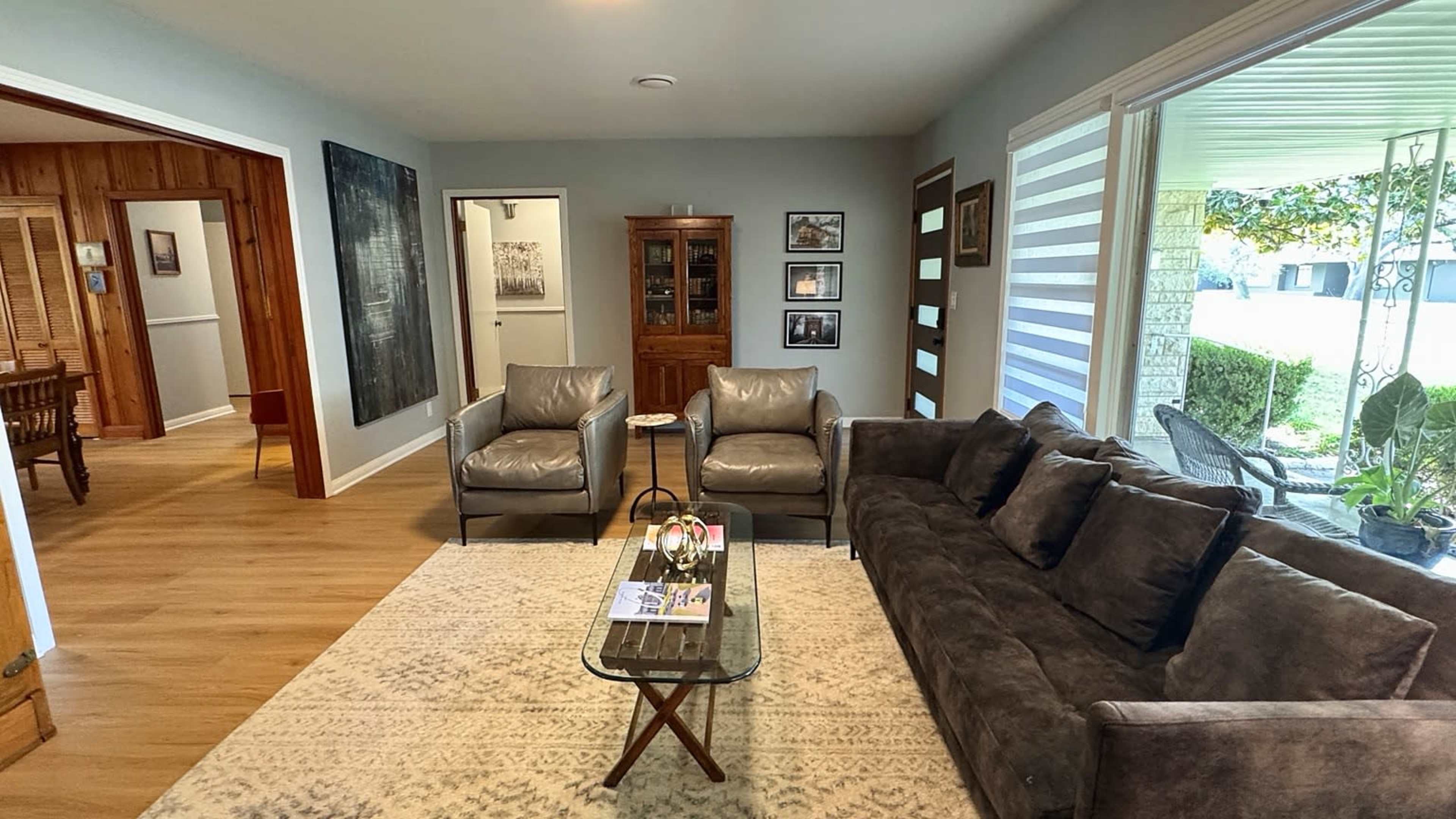 The living room features a gray sofa and armchairs, a glass coffee table, and is connected to adjacent rooms through an open layout.