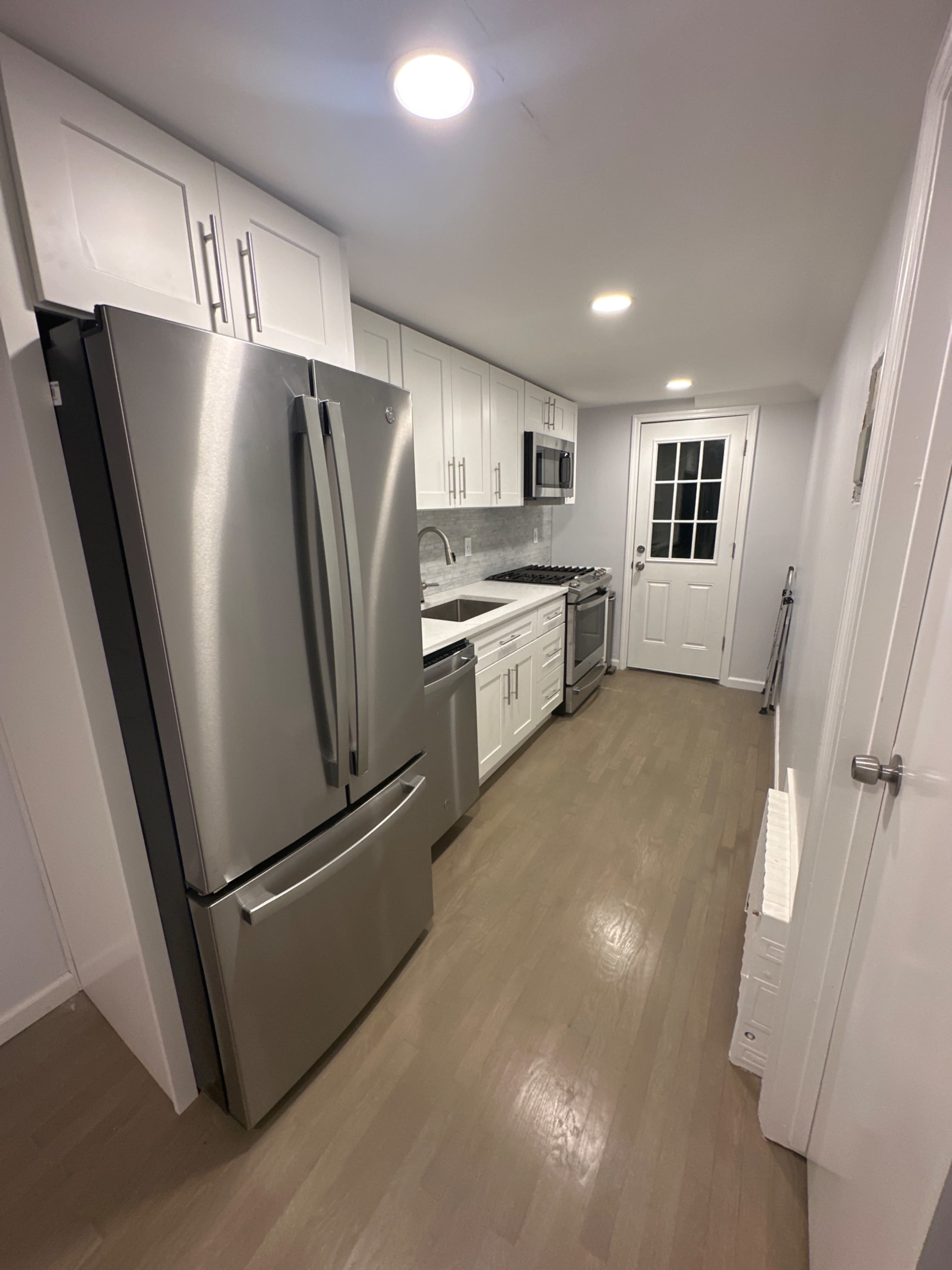 The image shows a modern kitchen with stainless steel appliances, white cabinetry, and light-colored flooring.