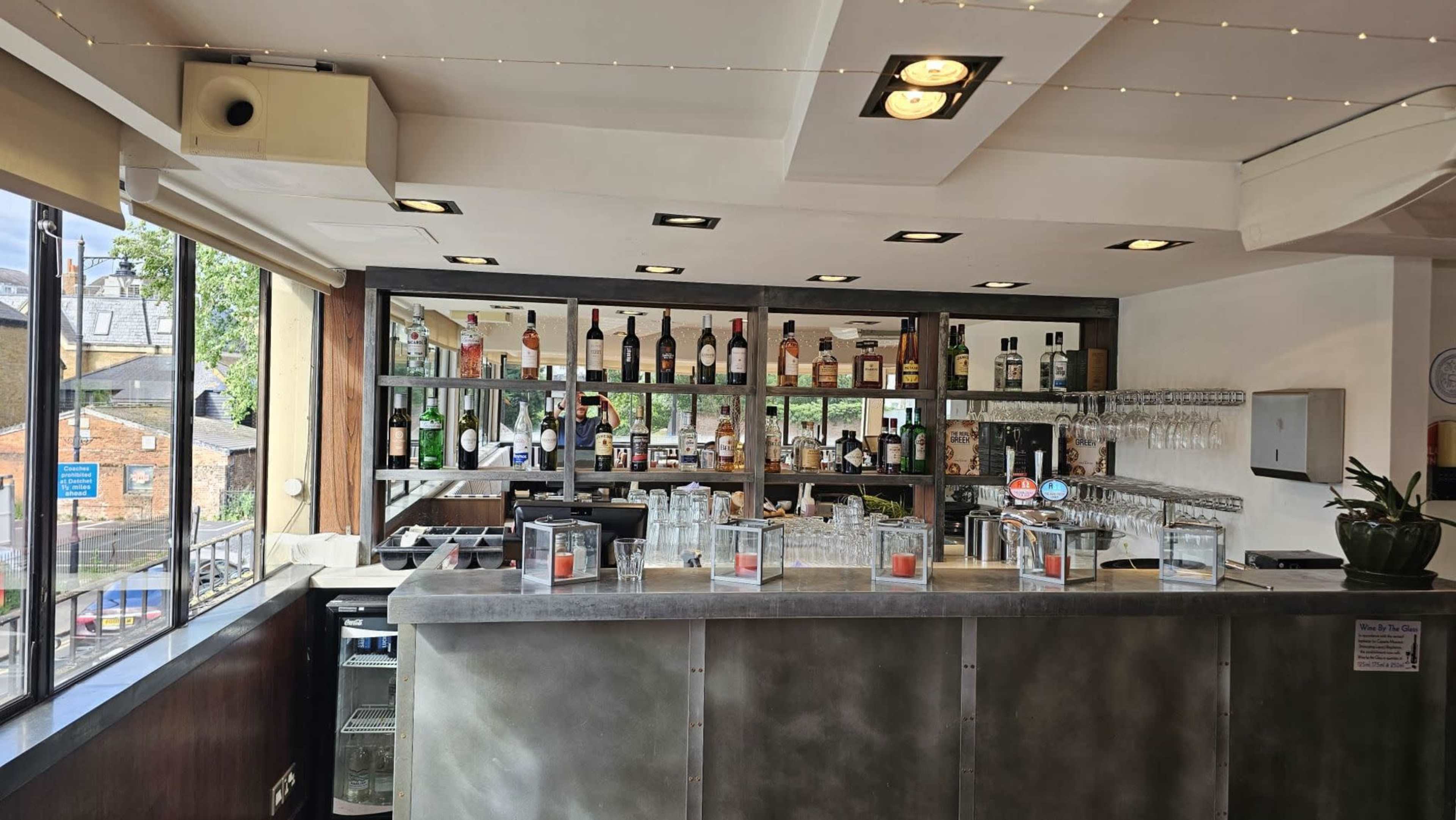 The image shows a well-lit bar area with shelves displaying various bottles of liquor and a counter with glassware.