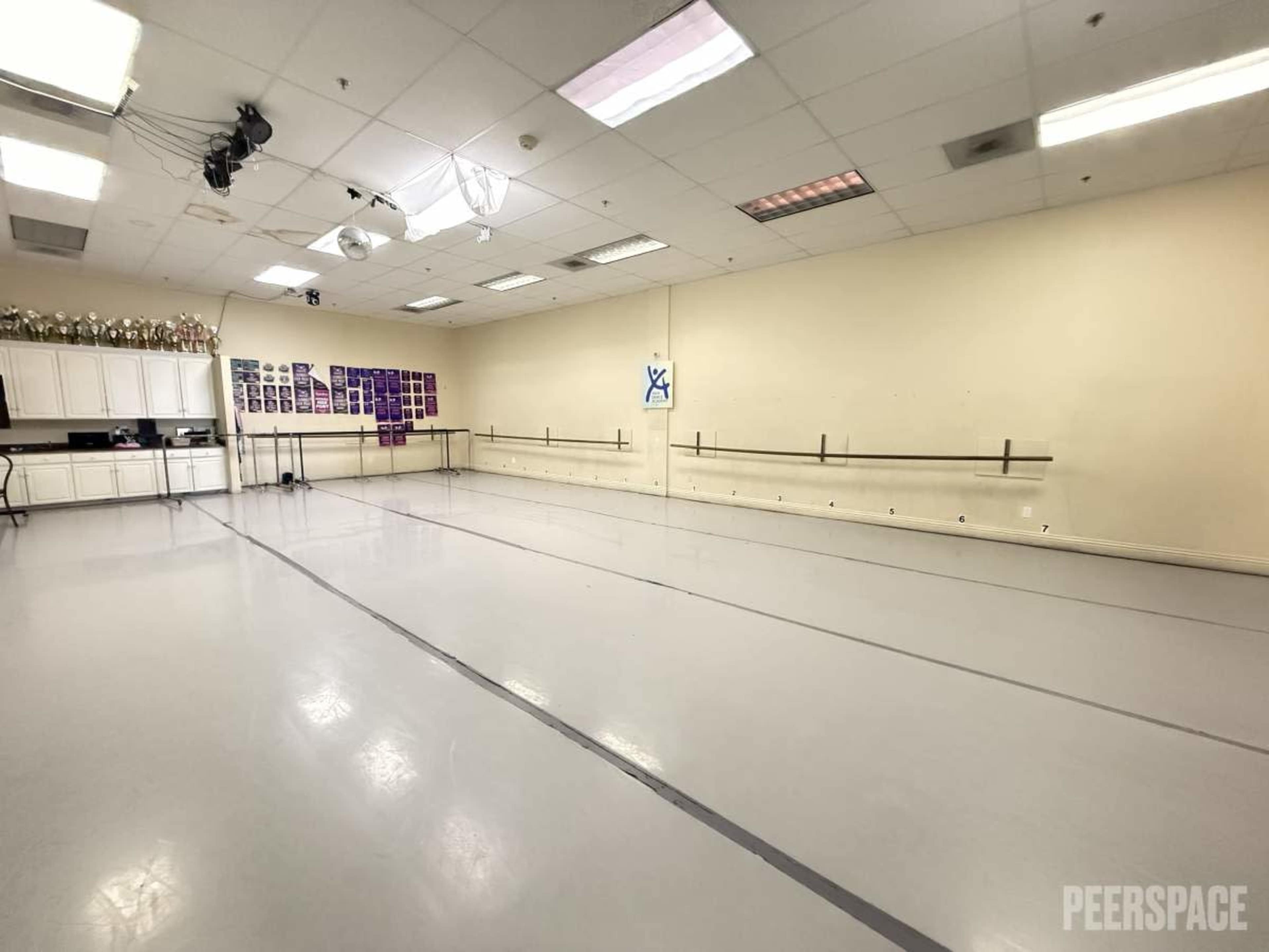 The image shows a spacious dance studio with a polished floor, wall-mounted ballet bars, and large mirrors.