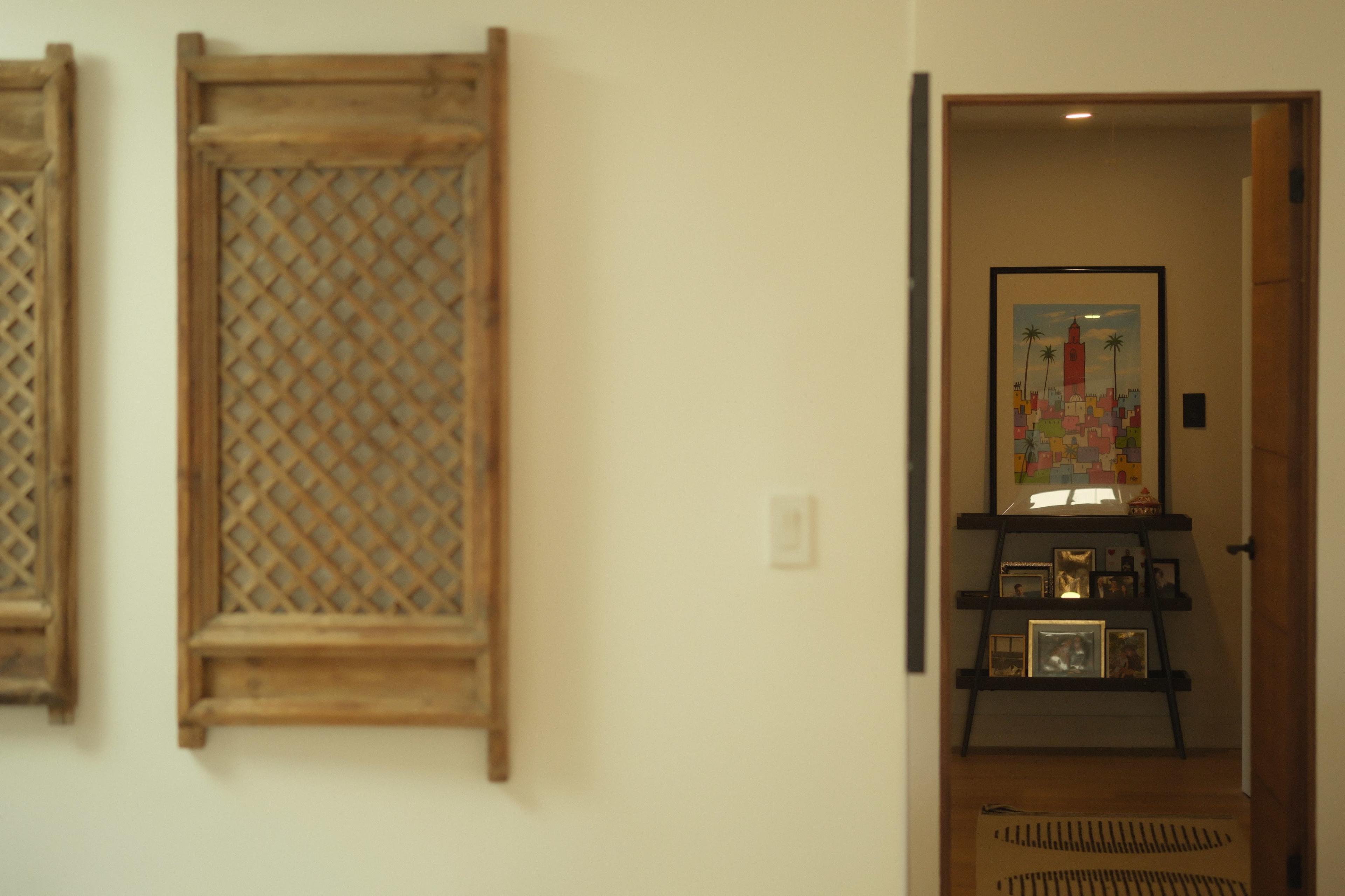 The image shows a hallway with wooden lattice wall decorations on the left and a framed art piece displayed on an easel at the end of the corridor.