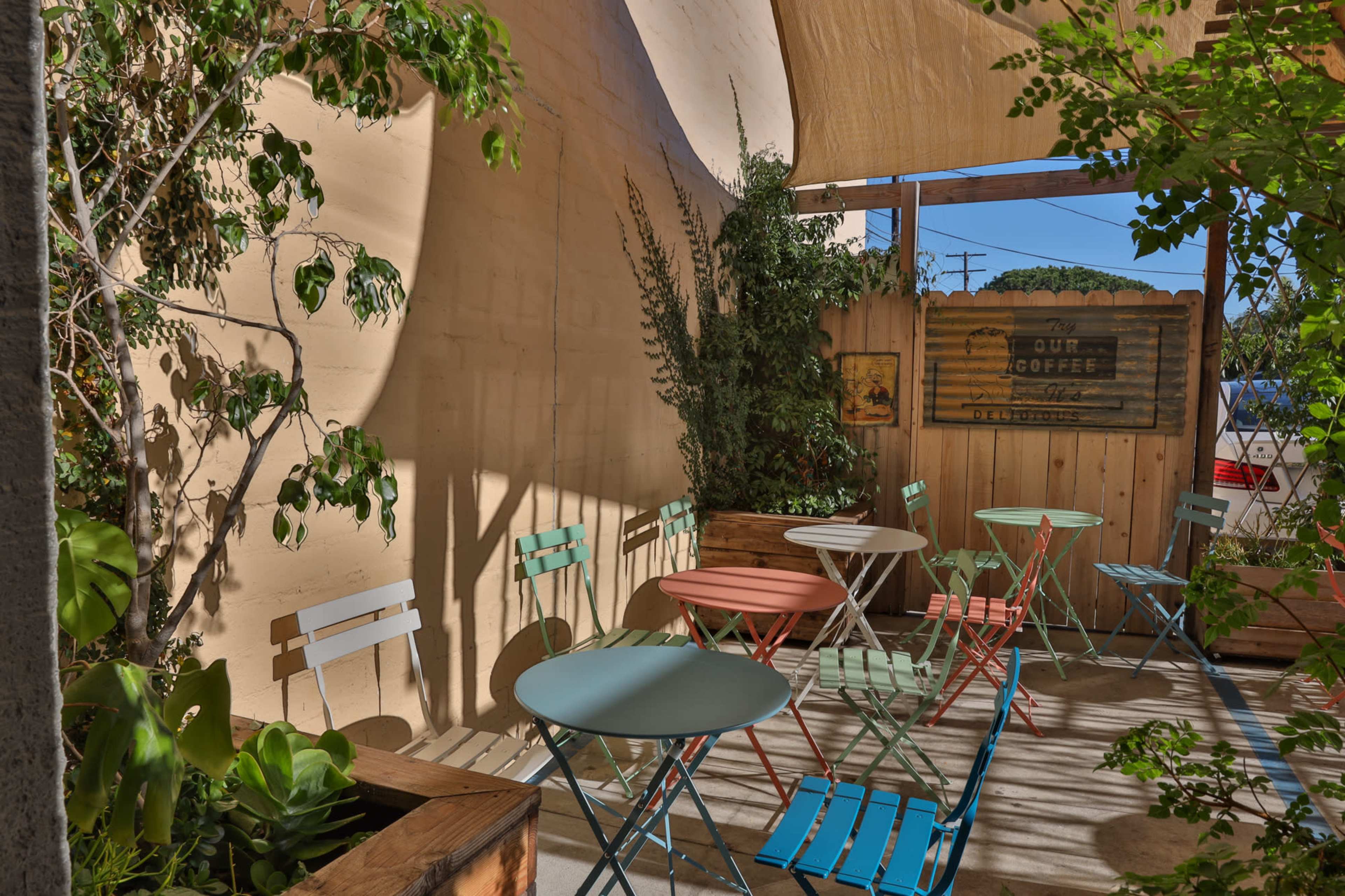 A small outdoor café area with colorful metal chairs and tables surrounded by greenery and wooden fencing.