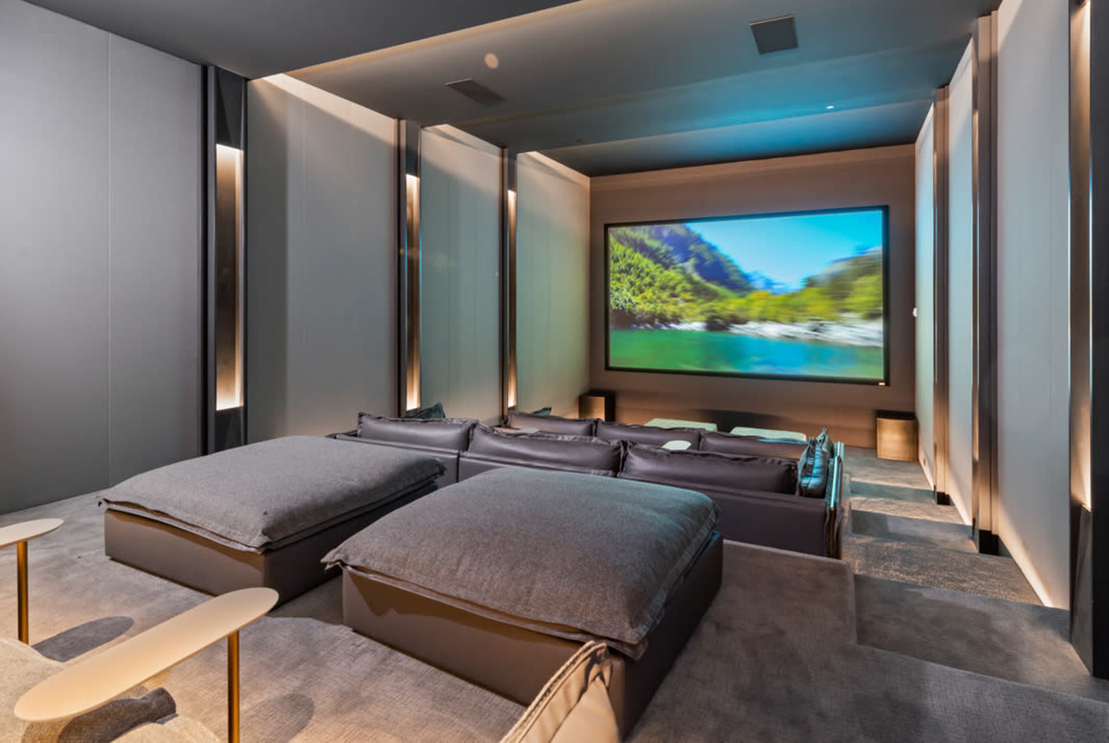 A modern home theater room with large cushioned seats facing a large screen displaying a nature scene.