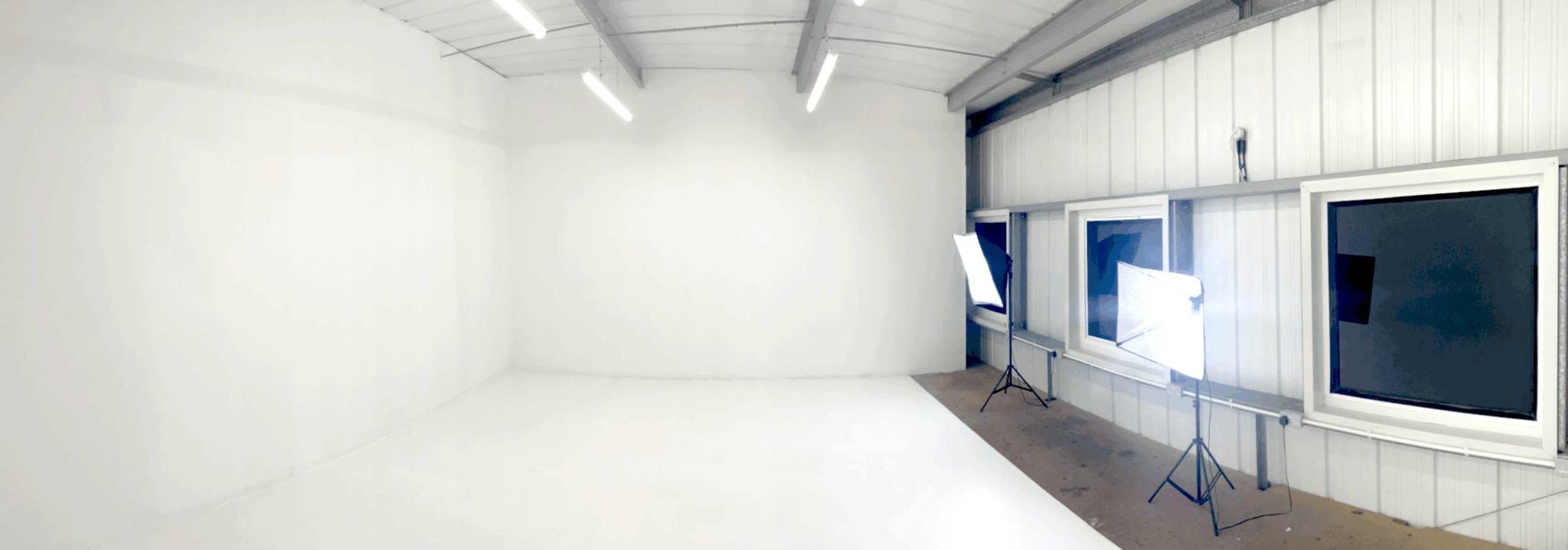 The image shows a spacious, empty room with white walls and bright lighting from studio lamps.