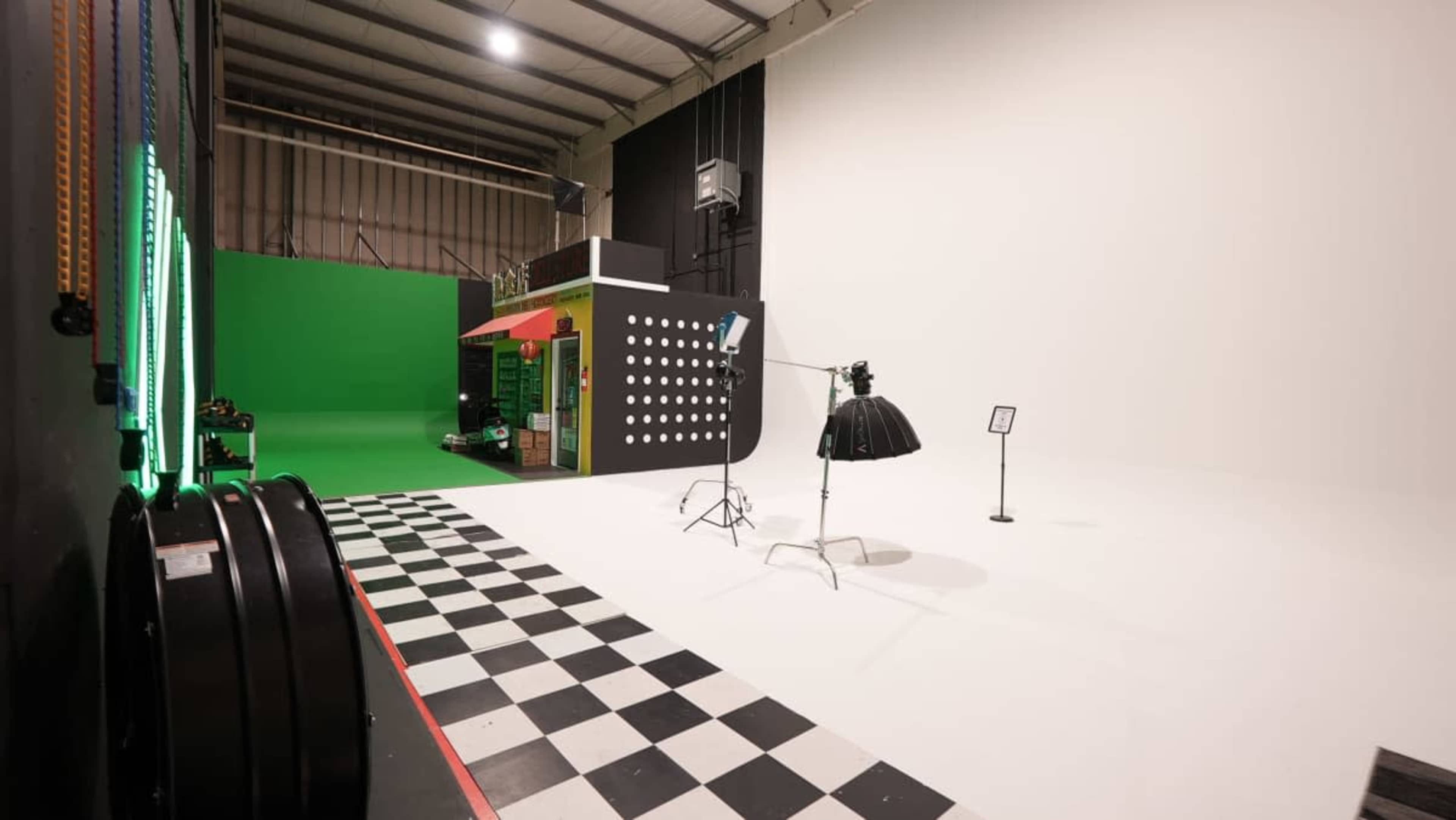 The image shows a photography studio with a large green screen area, a section featuring a colorful backdrop with polka dots, and a black and white checkered floor.