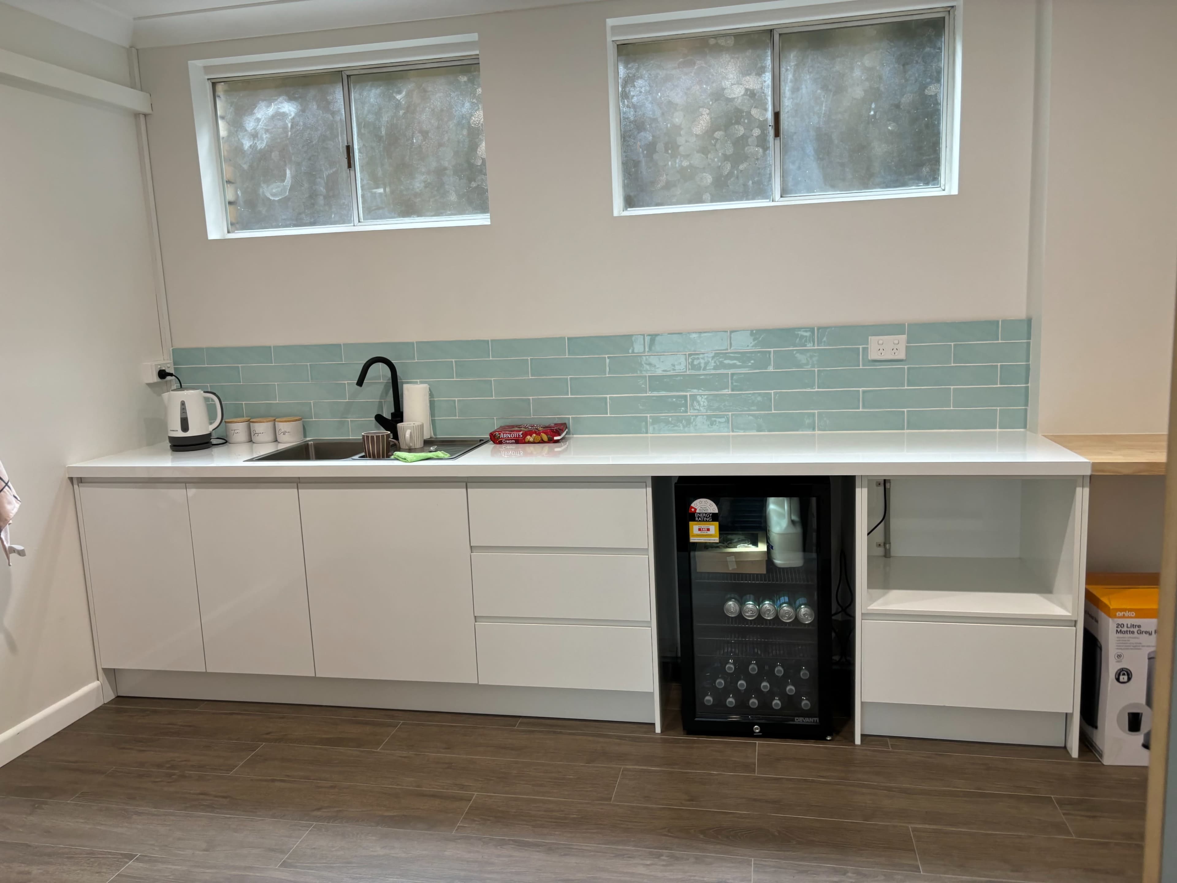 The image shows a modern kitchen with white cabinetry, a light turquoise tiled backsplash, and a small beverage fridge beside the sink.