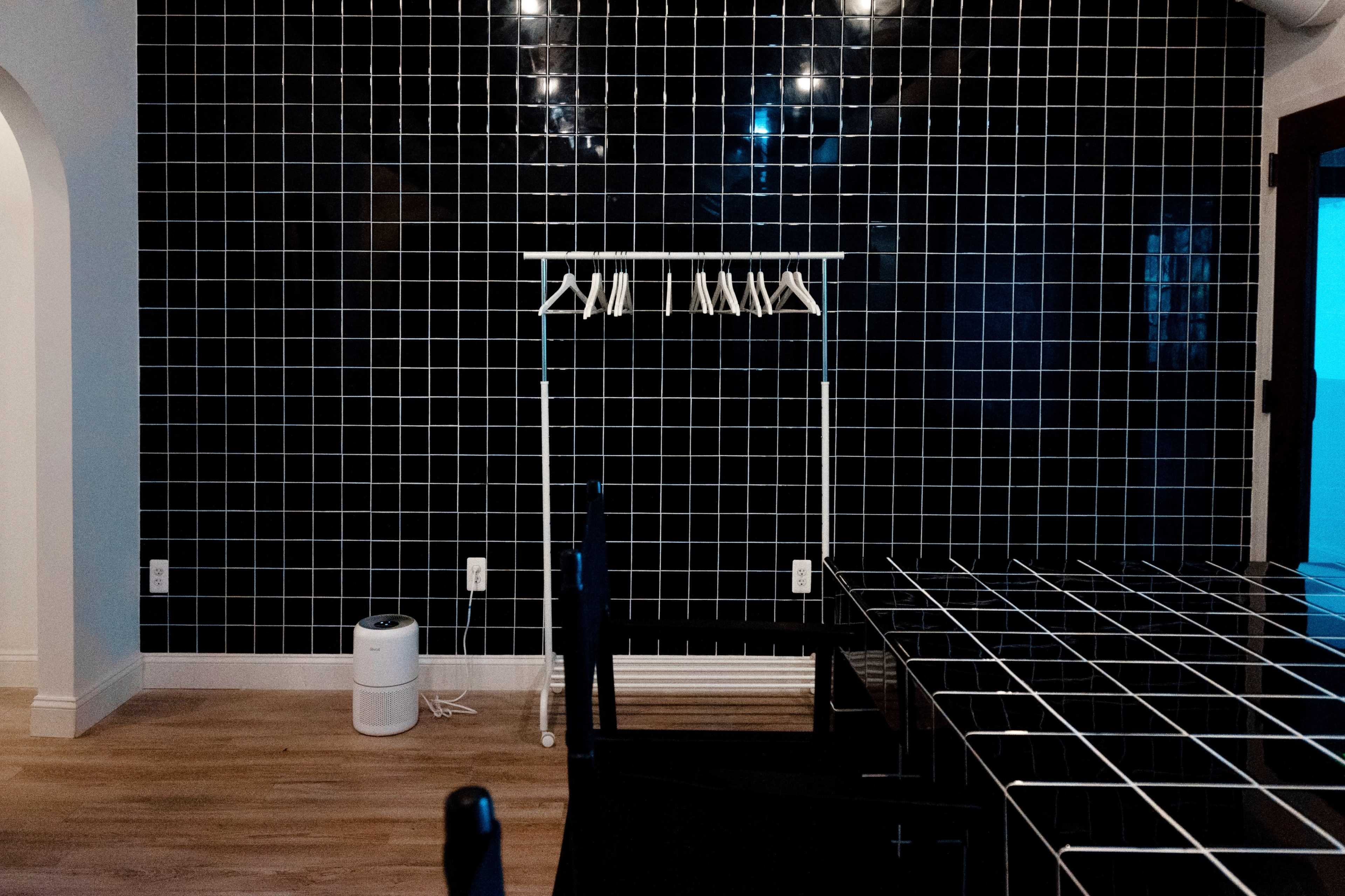 A minimalist room with a black tiled wall, a white clothing rack, a small air purifier, and a table with a grid pattern.