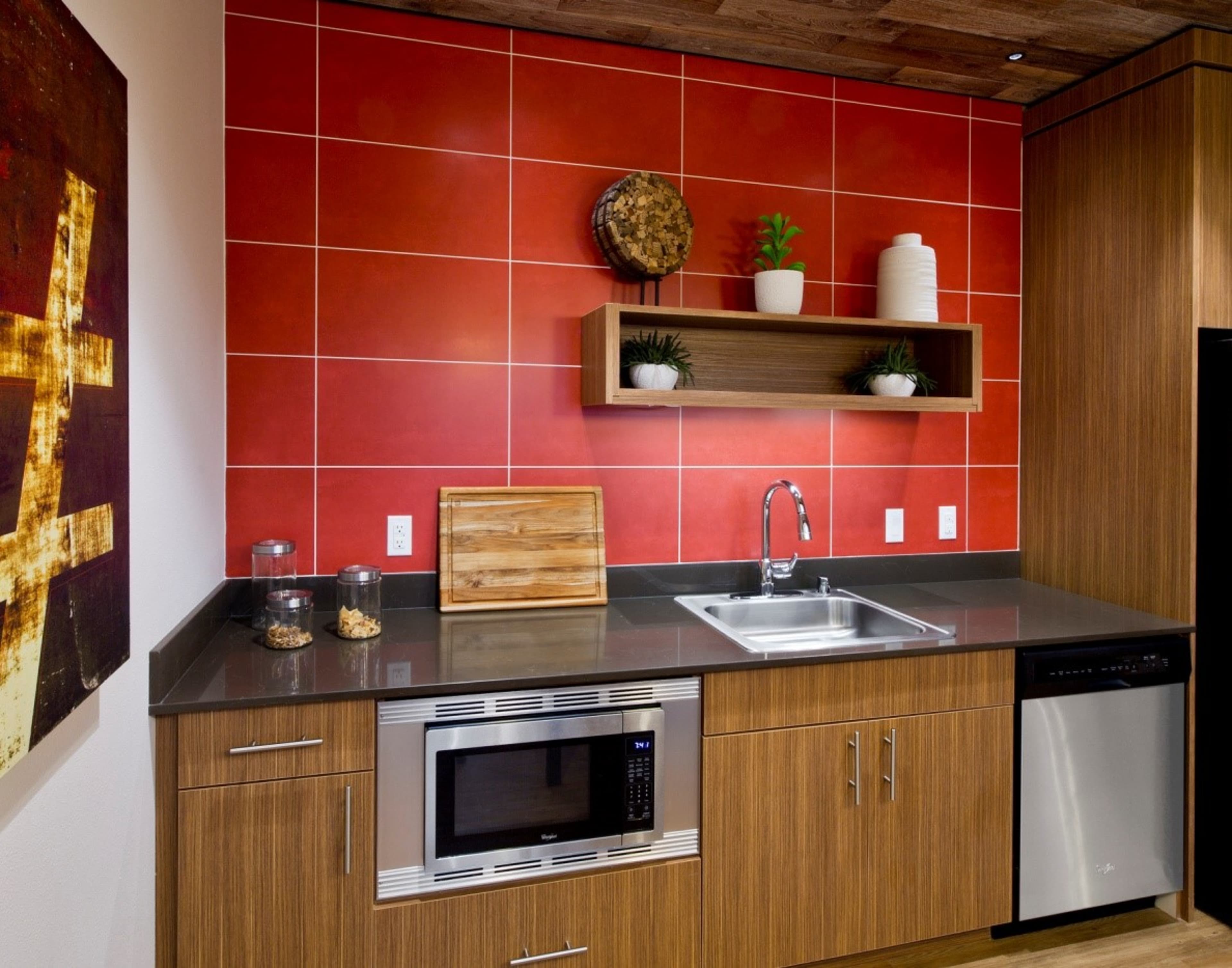 The kitchen features red tiled walls, wooden cabinets, a stainless steel sink with a modern faucet, and various kitchen appliances including a microwave and dishwasher.