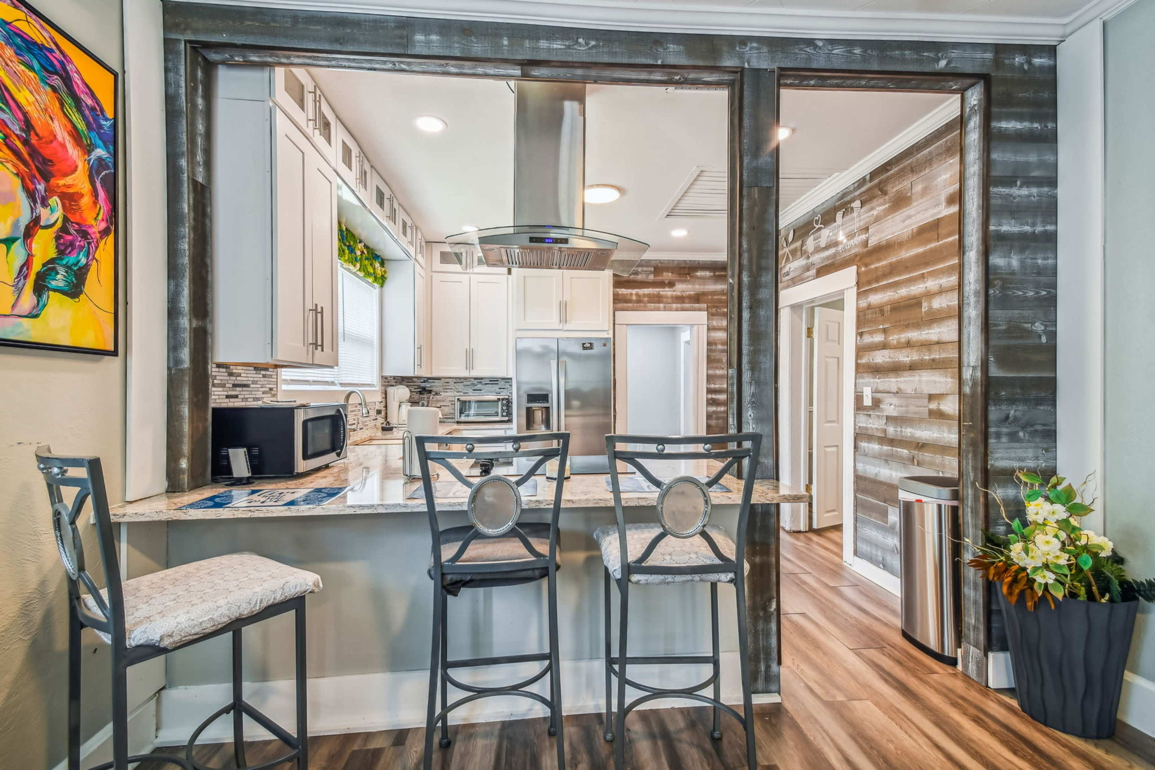 A modern kitchen with a bar area featuring three high stools, stainless steel appliances, and a window above the sink.