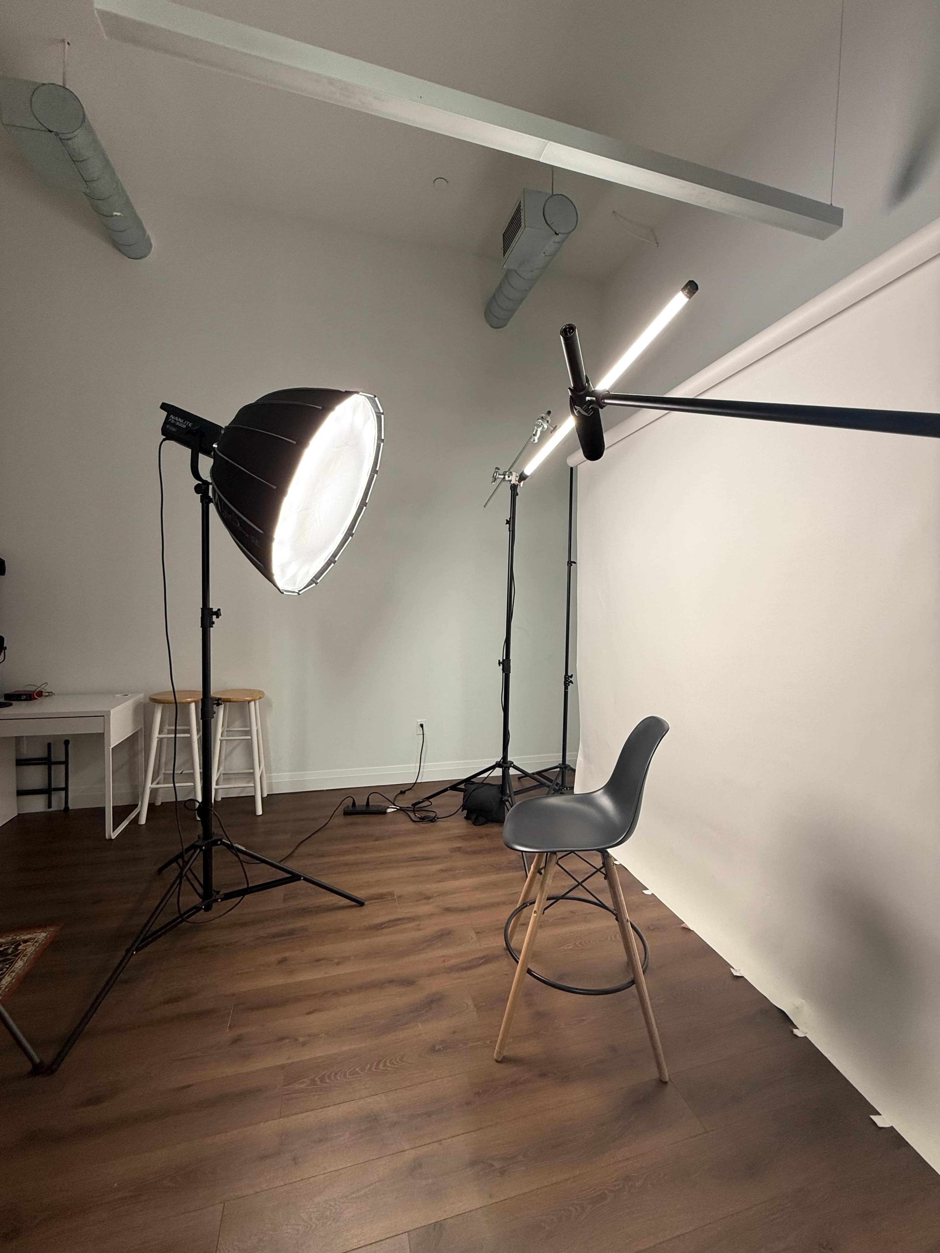 The image depicts a photography studio setup featuring a gray chair, a large softbox light, and a white backdrop.