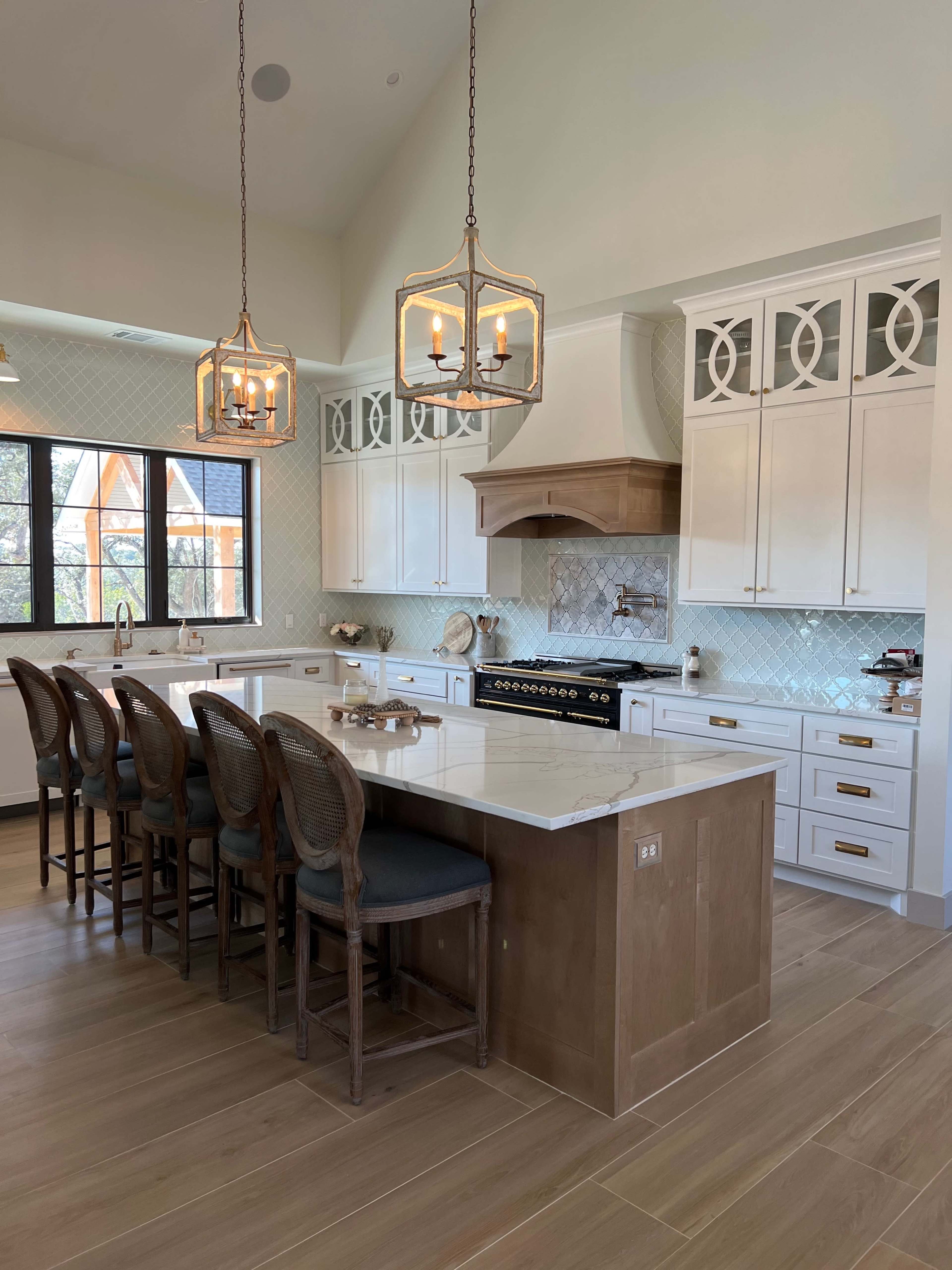 A modern kitchen with a large island, seating for several people, white cabinets, and pendant lighting.