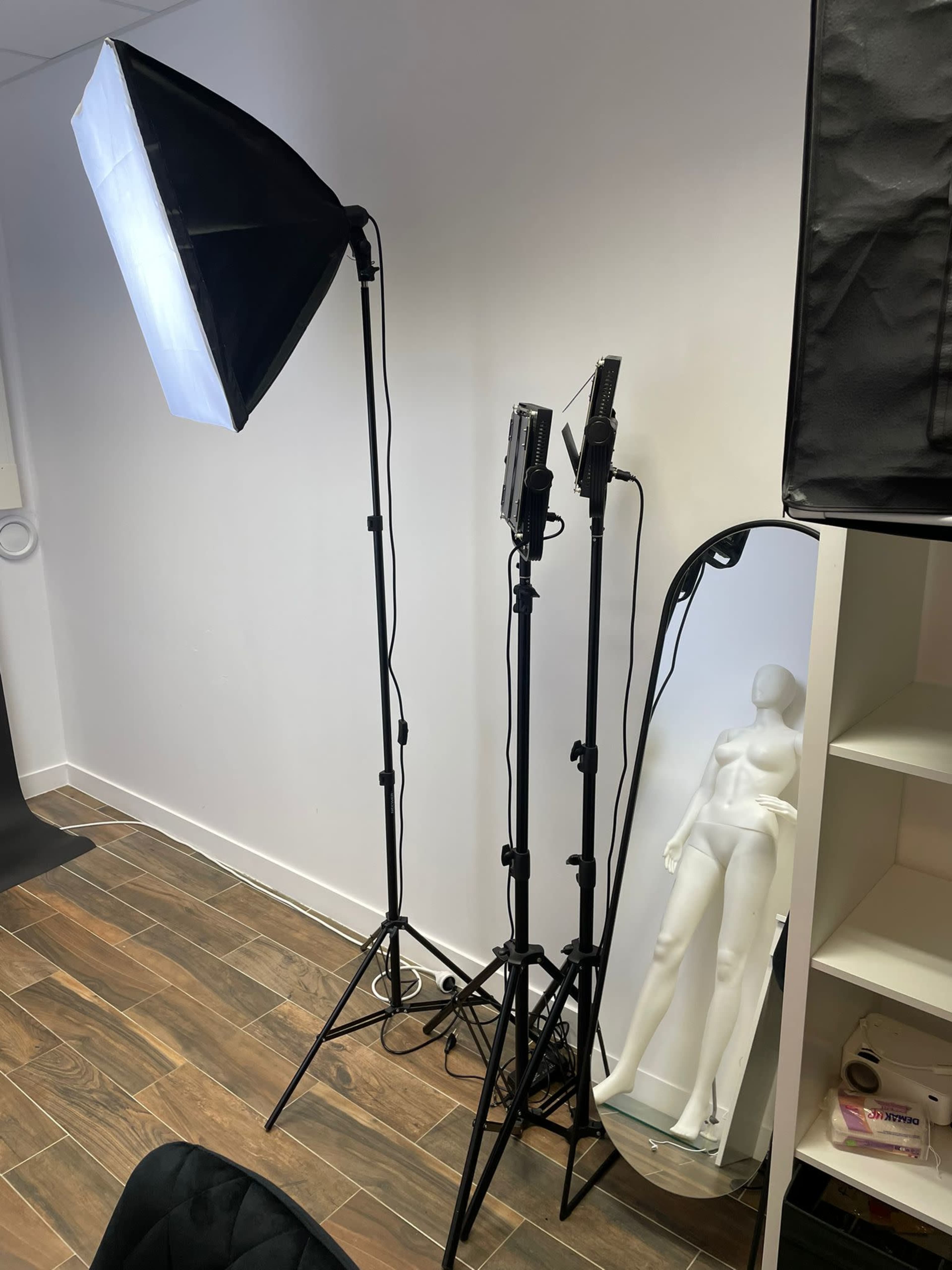 A photography setup with two softbox lights and a mannequin next to a full-length mirror against a white wall.