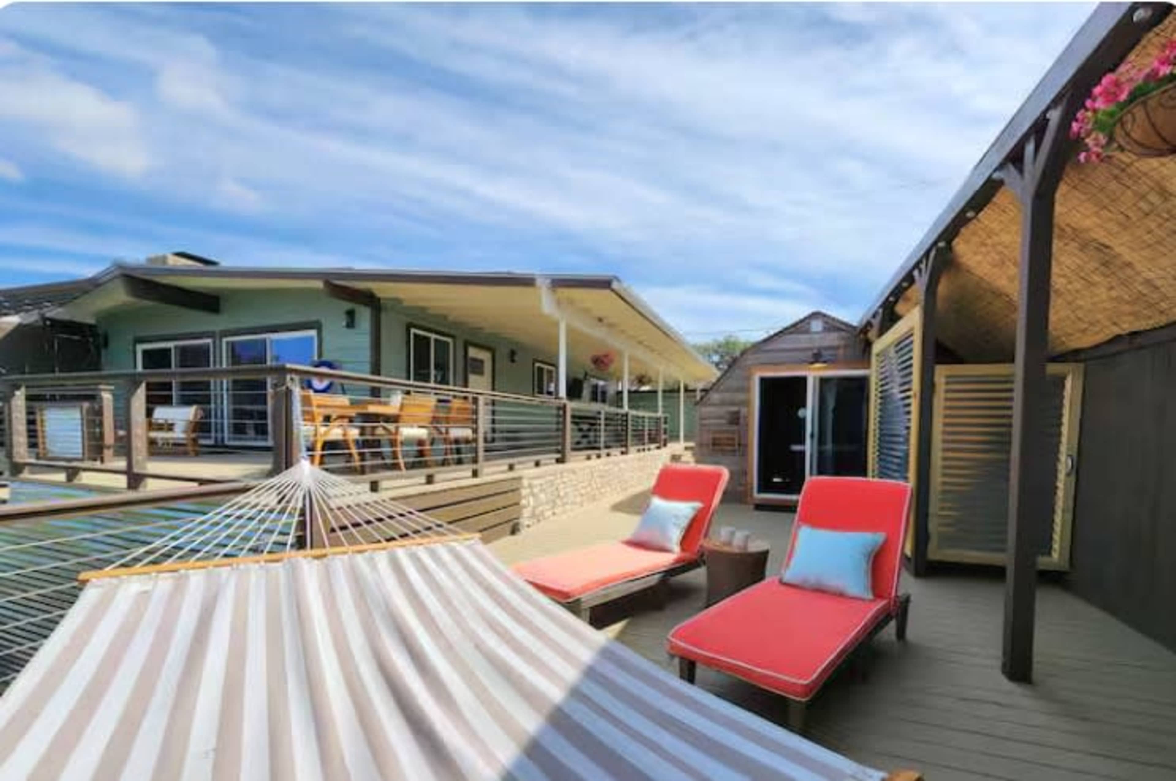 A spacious deck with two red lounge chairs and a hammock overlooks a building with blue and wooden accents.