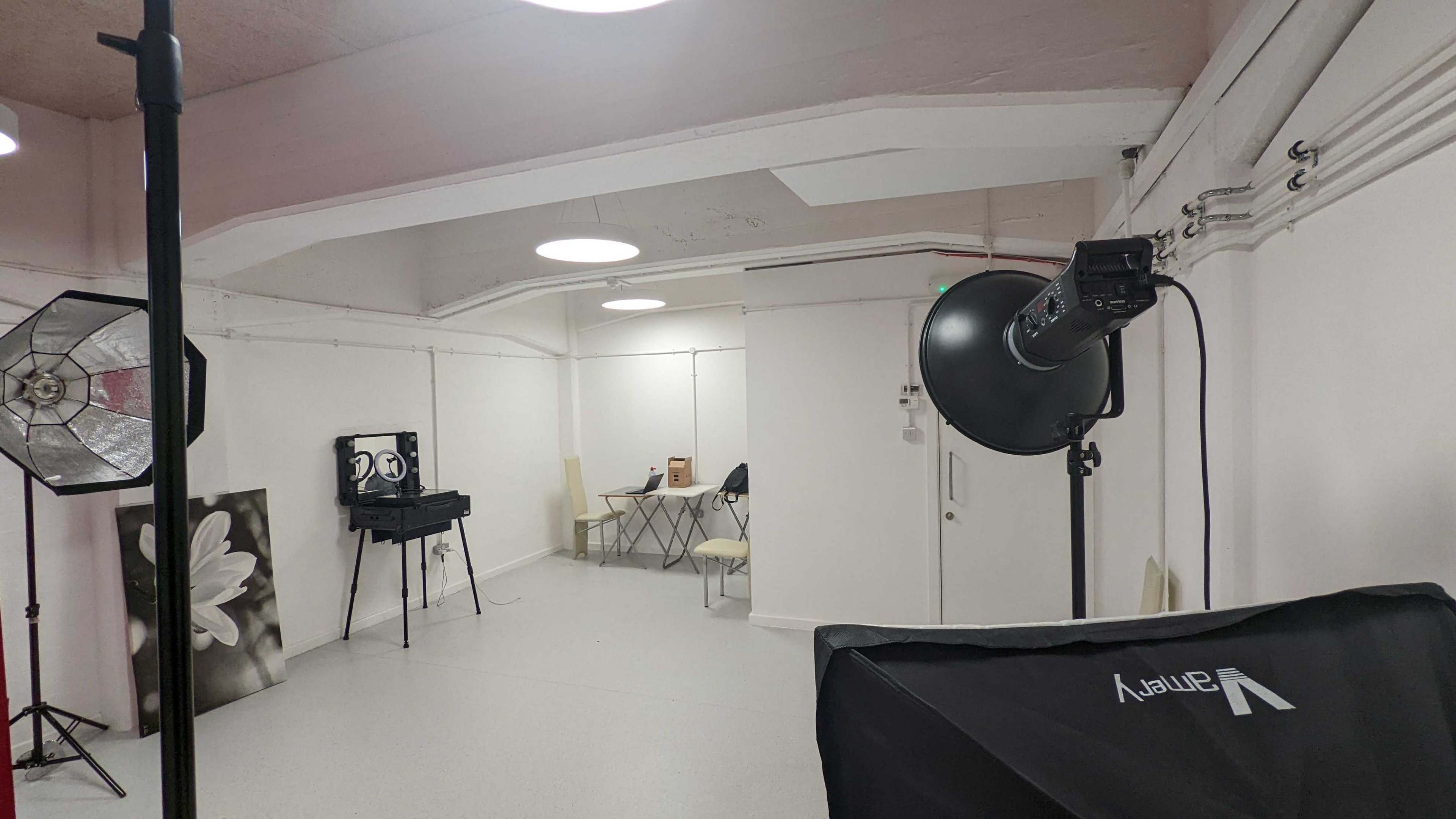 An empty studio space equipped with lighting, a table, and chairs against a light-colored wall.