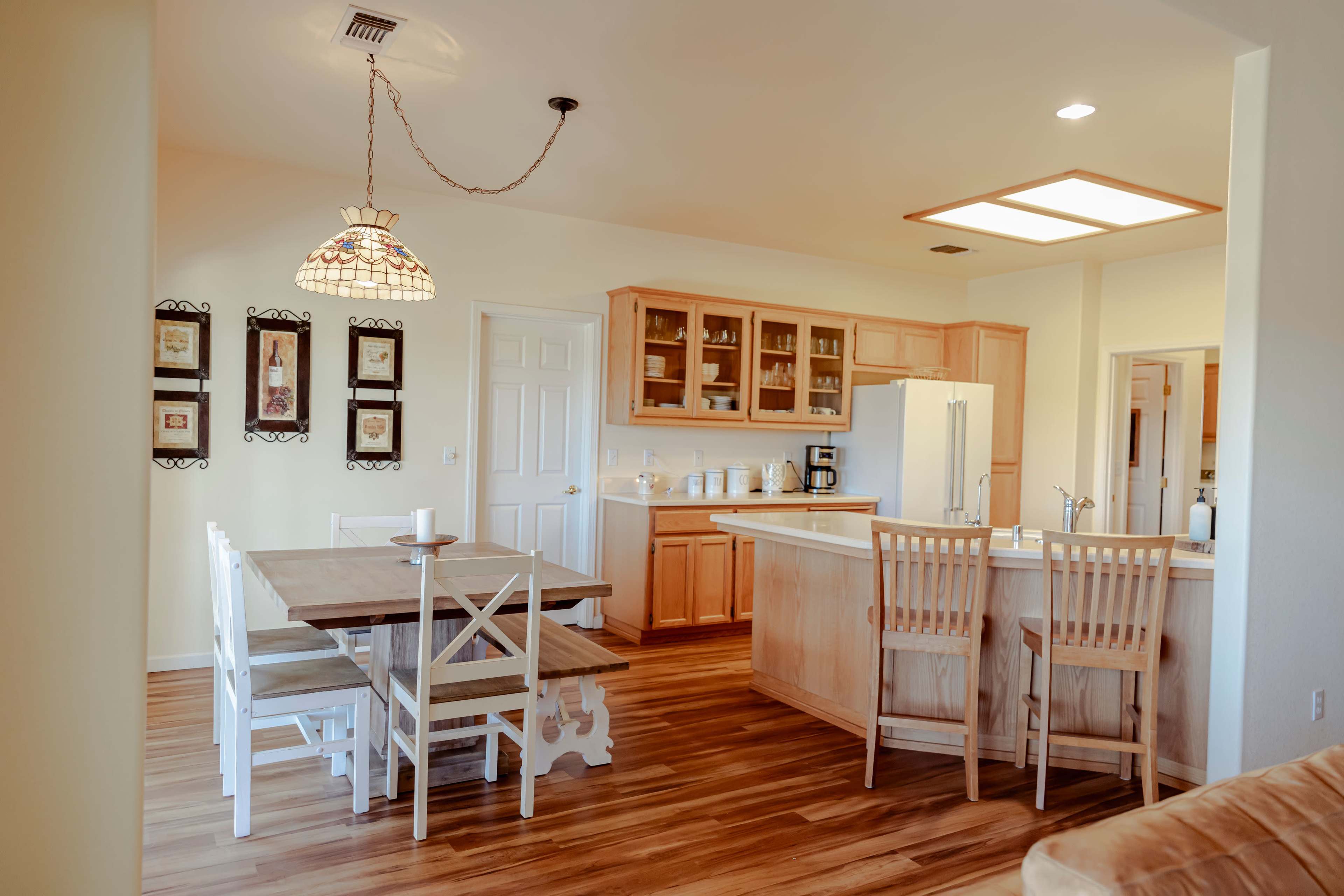 A modern kitchen and dining area with wooden cabinets, a central island, a large table with white chairs, and a pendant light.