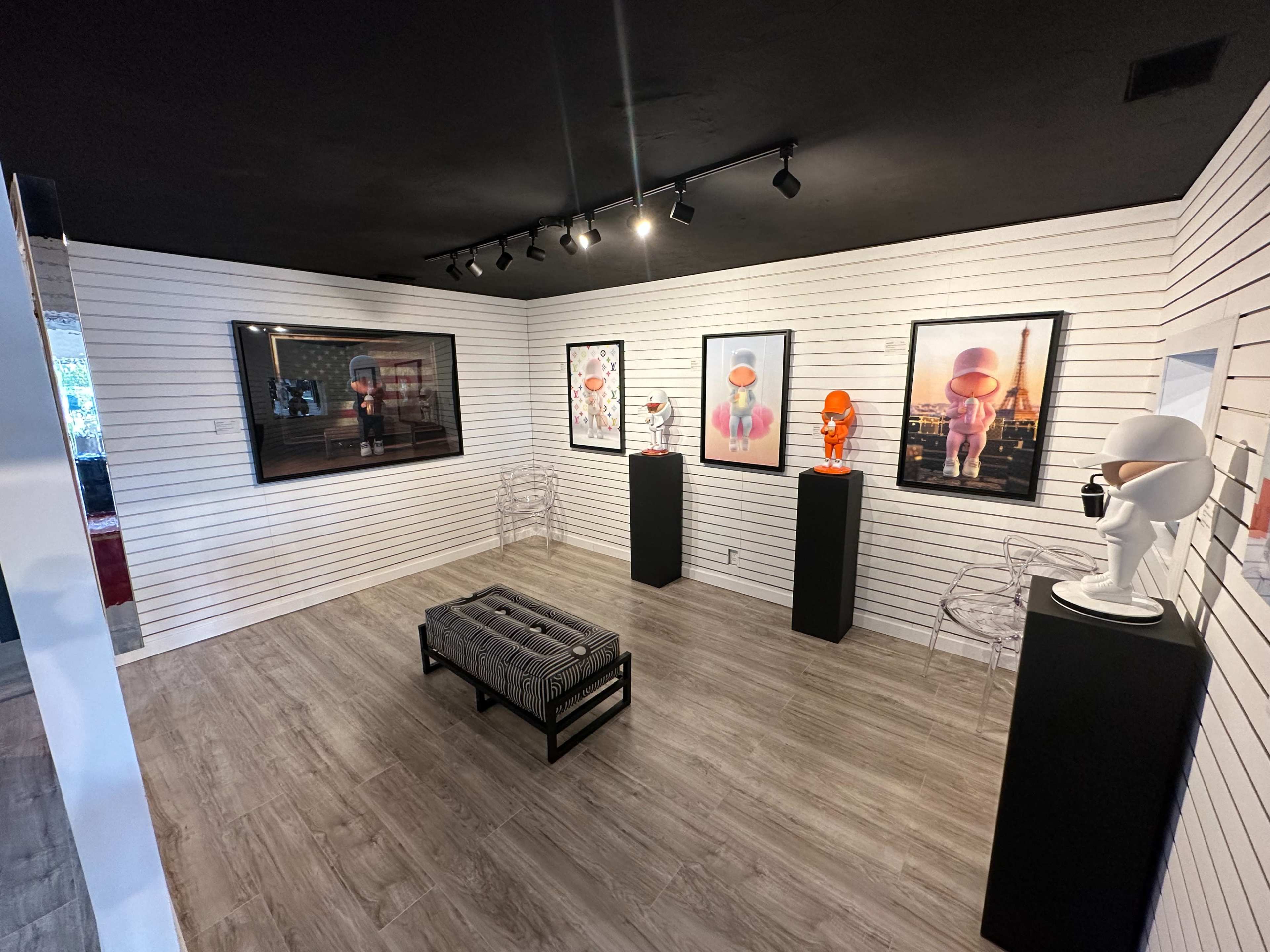 An art gallery with a minimalist design, featuring framed artworks on white striped walls and sculptures displayed on black pedestals.