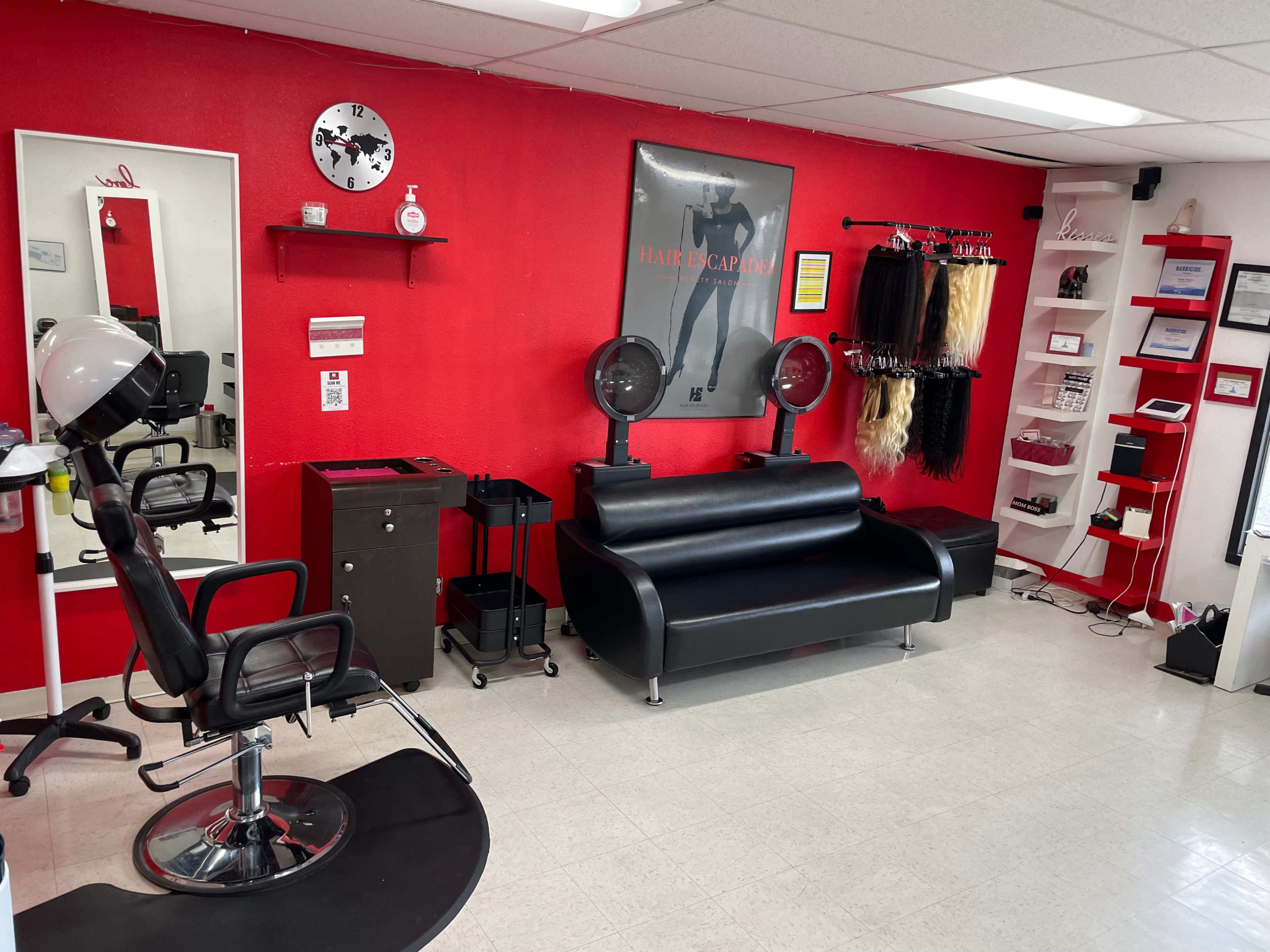 A hair salon featuring a black leather couch, styling chair, mirror, and various hair products displayed against a red wall.