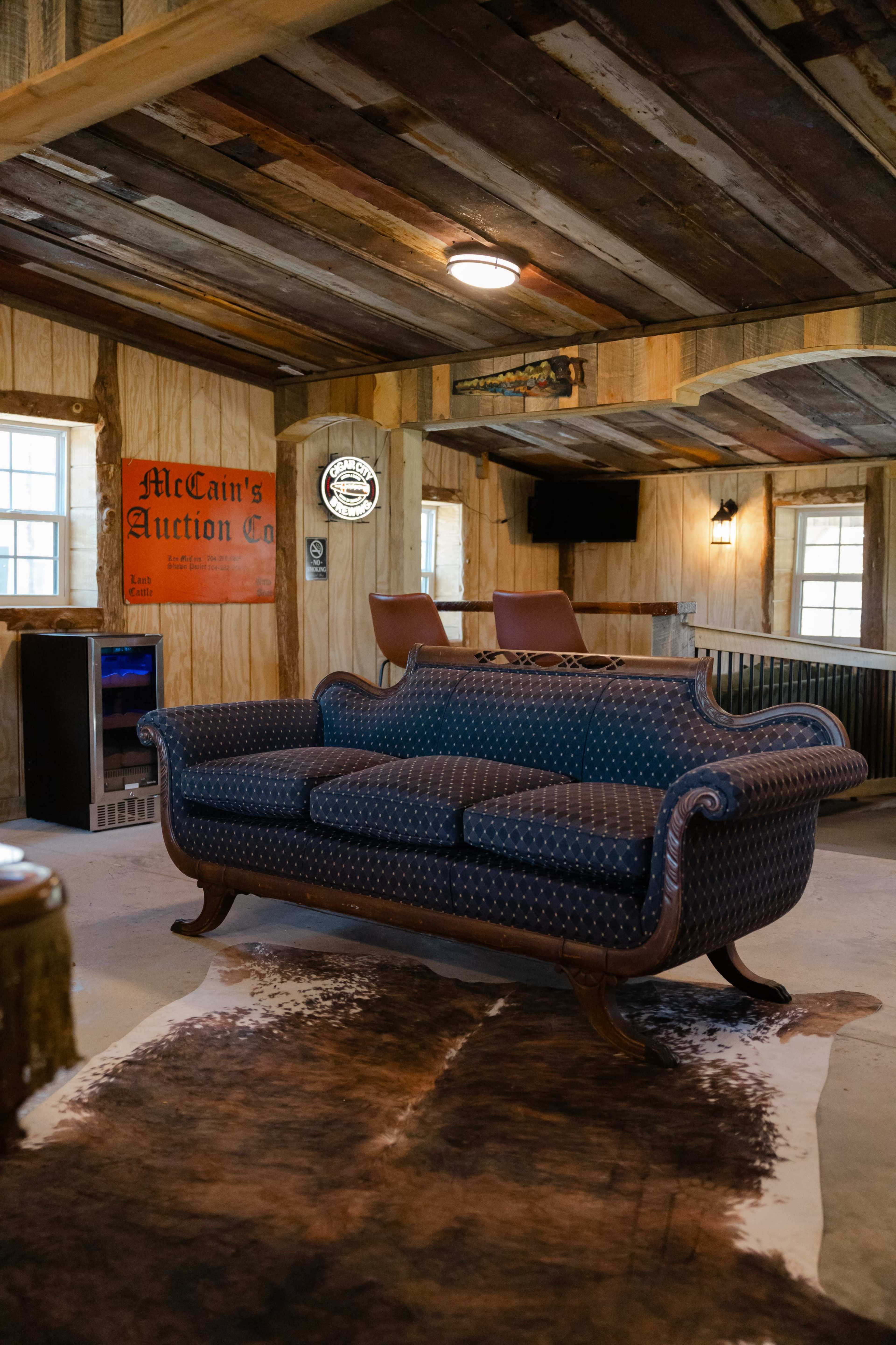 The image shows a vintage couch in a rustic interior space with wooden walls, a cowhide rug, and auction memorabilia on display.