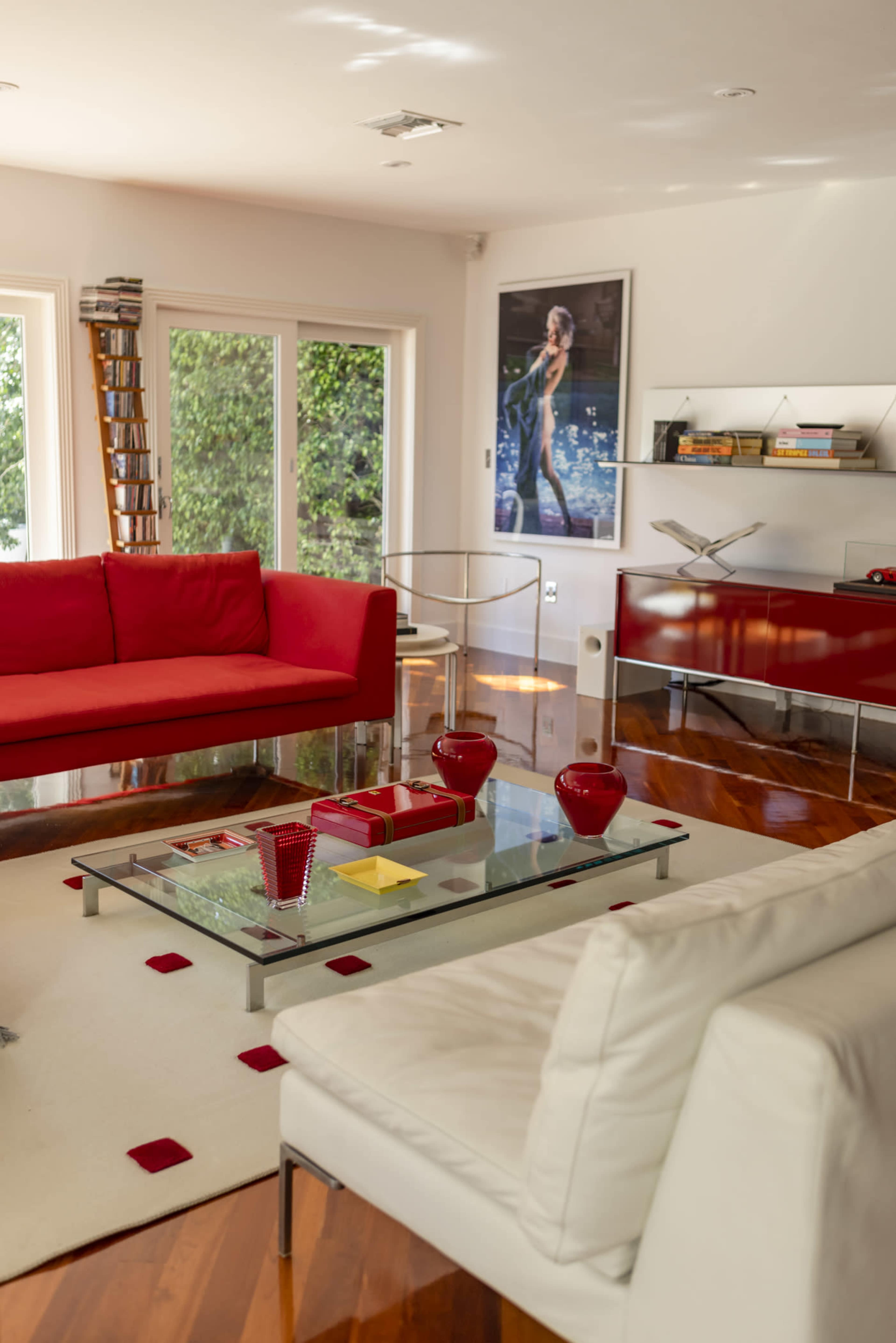 A modern living room features red and white sofas, a glass coffee table, and large windows that provide natural light.