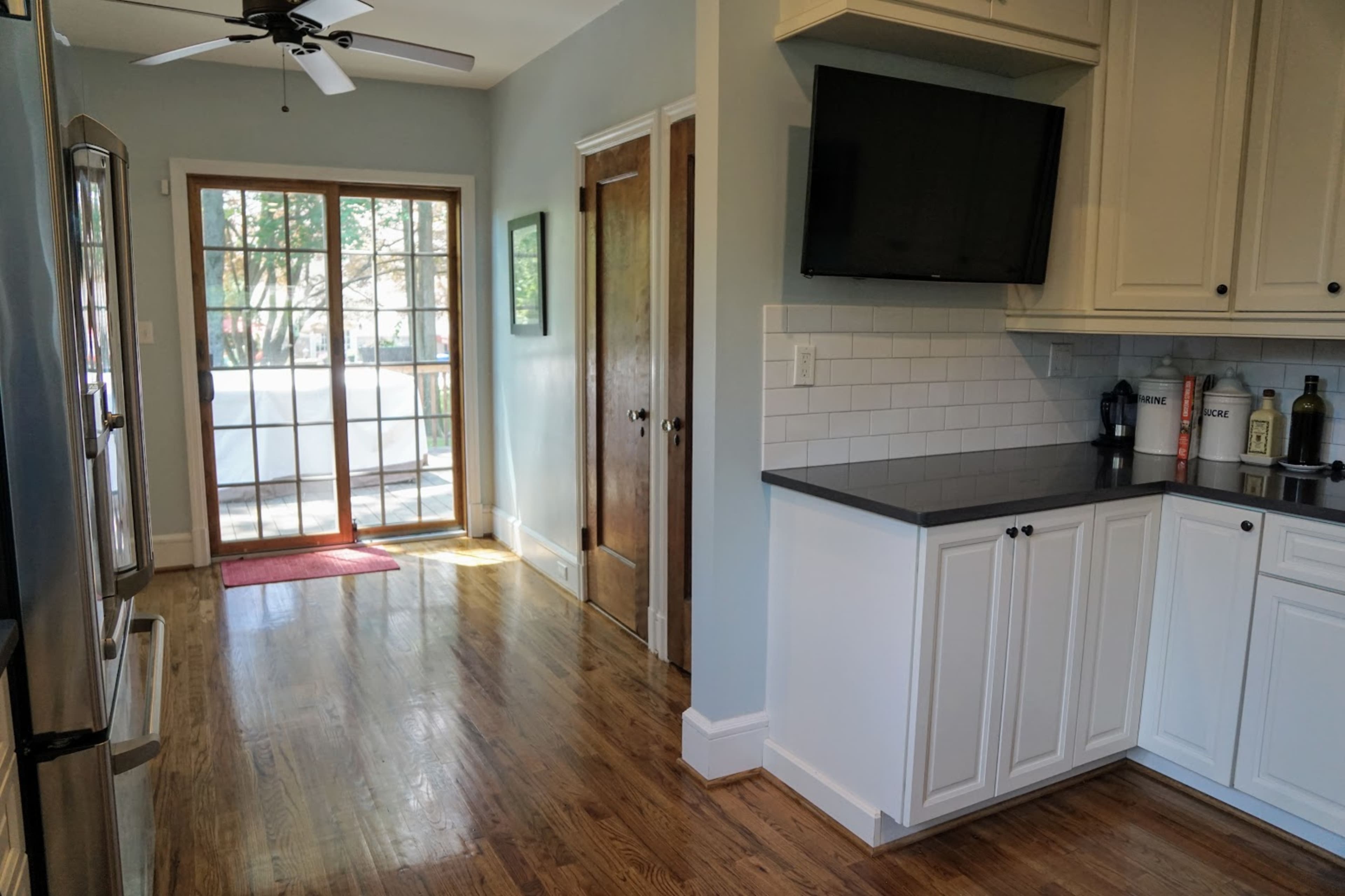 The image shows a kitchen with stainless steel appliances, white cabinetry, and a door leading to a porch, illuminated by natural light.