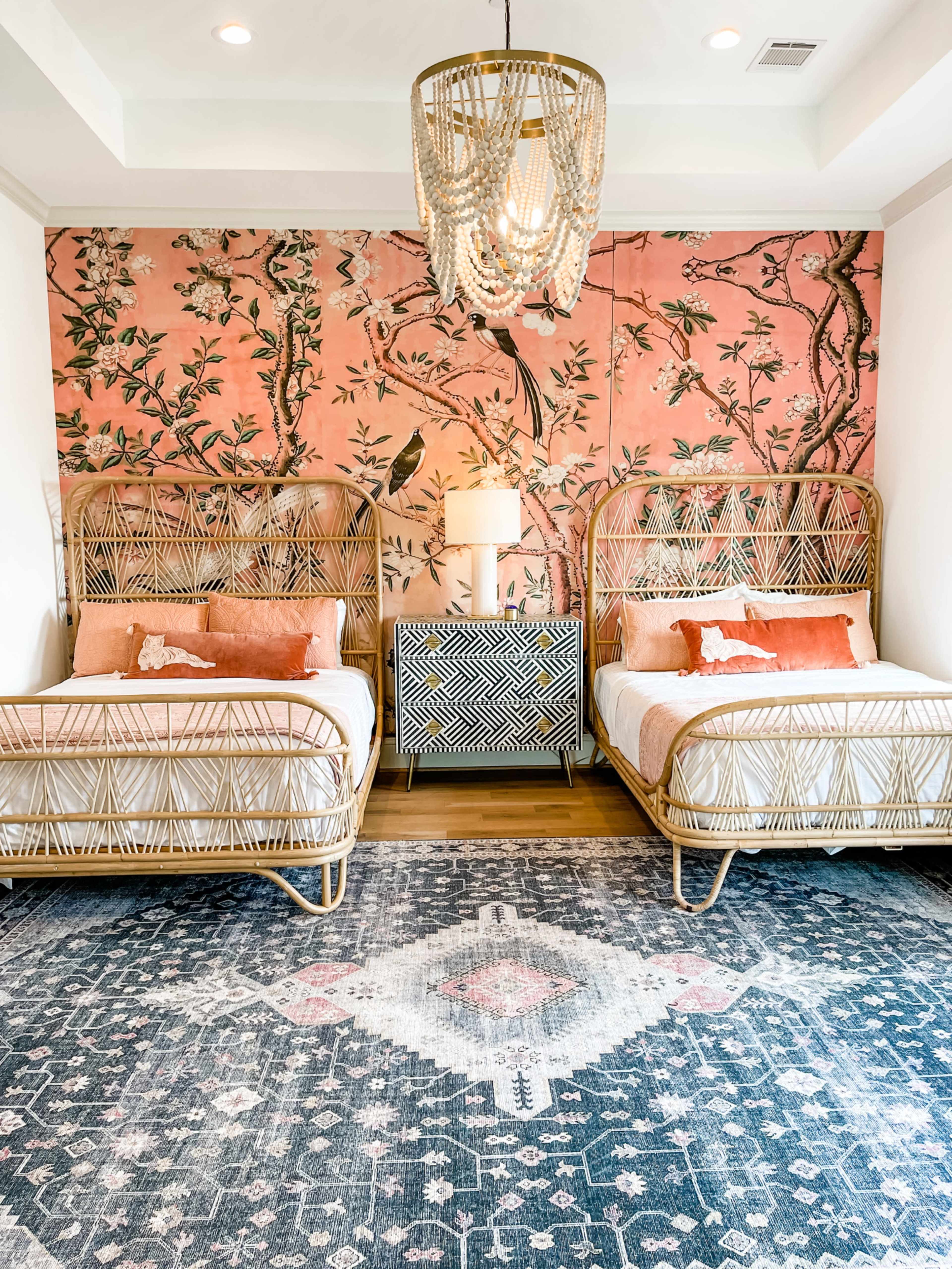 A bedroom with two wicker beds, a patterned area rug, and a floral wallpaper backdrop.