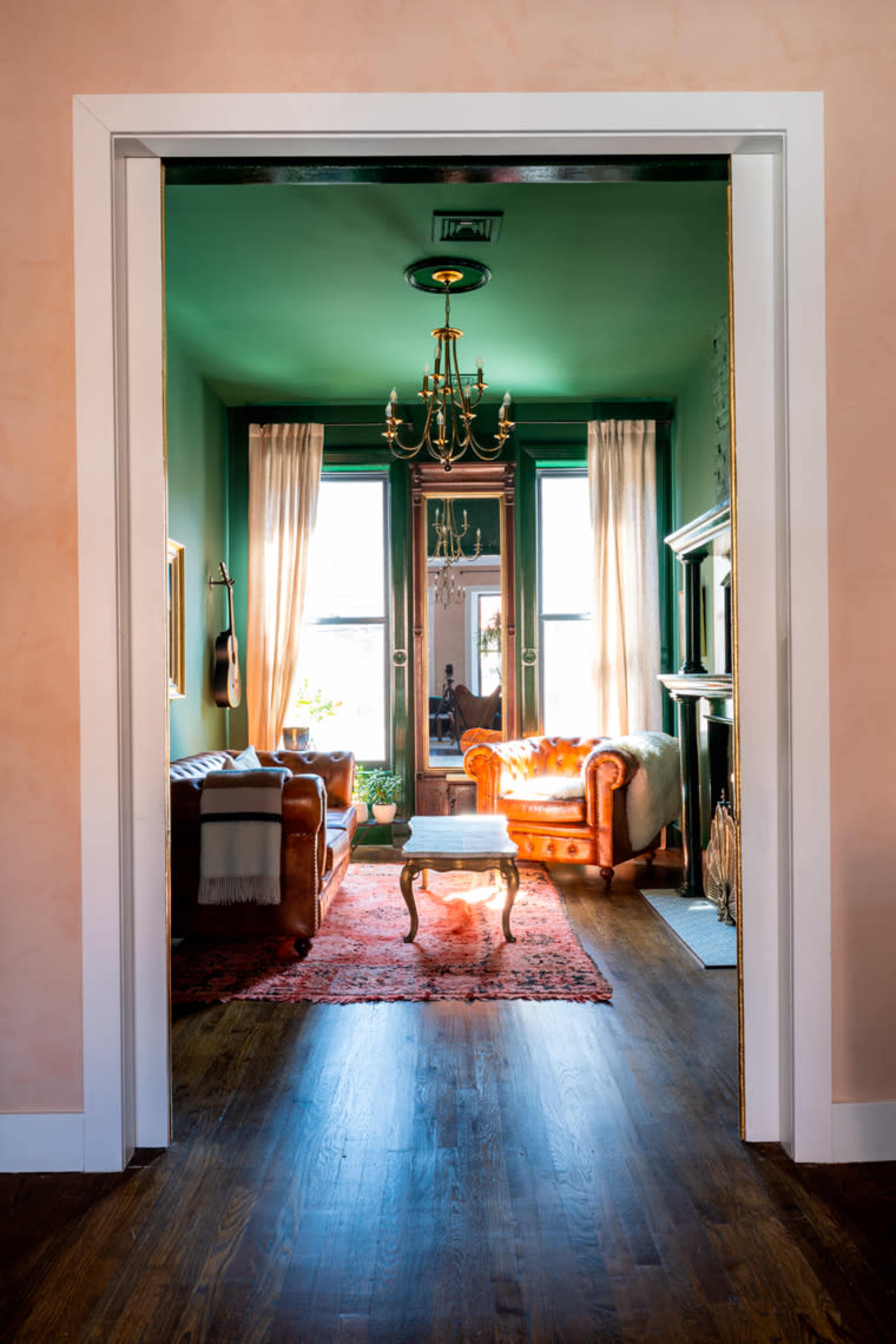A doorway frames a green living room featuring a leather sofa, a coffee table, and a chandelier.