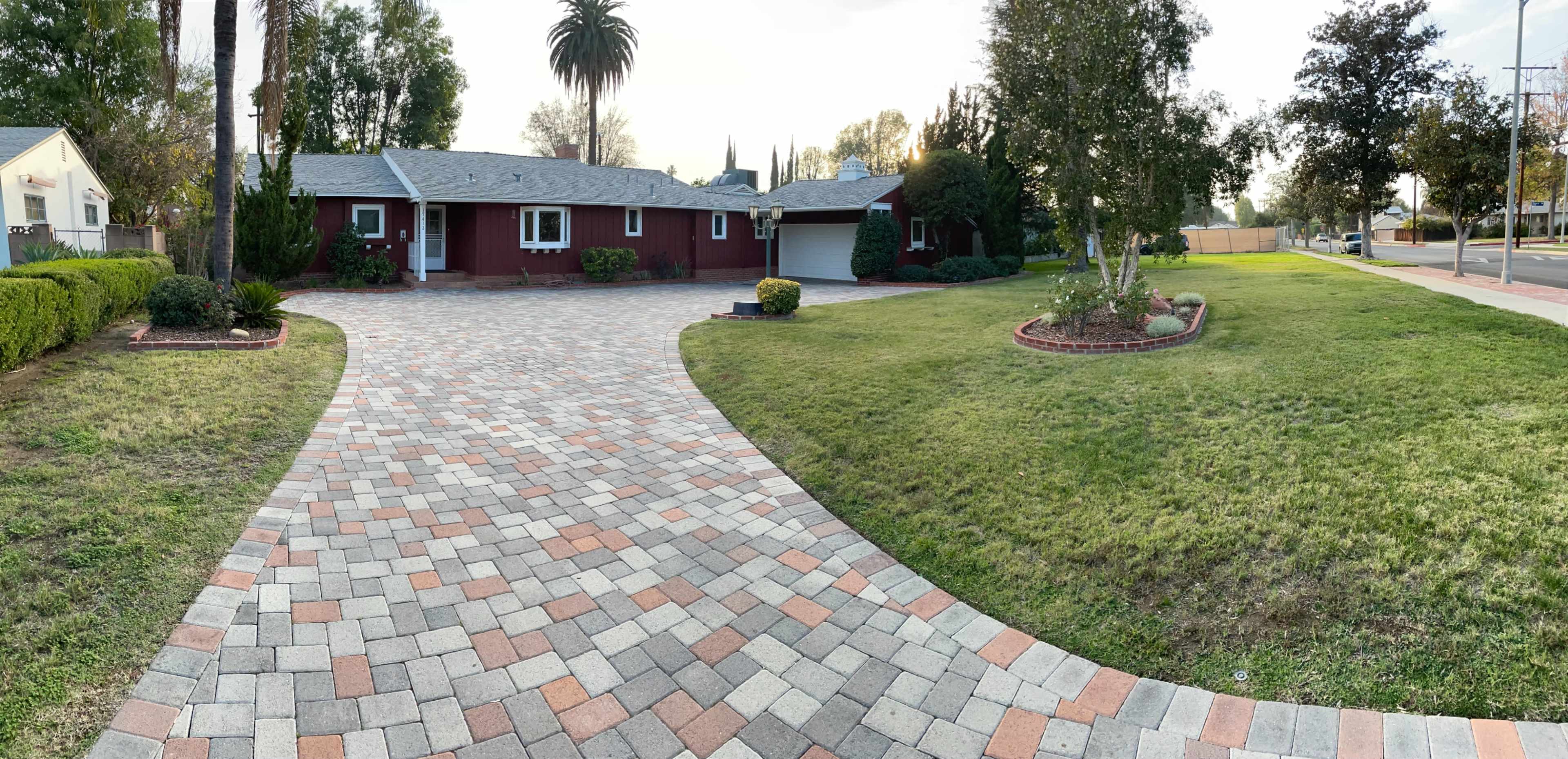 A residential front yard with a paved driveway leading to a house, surrounded by landscaped grass and bushes.