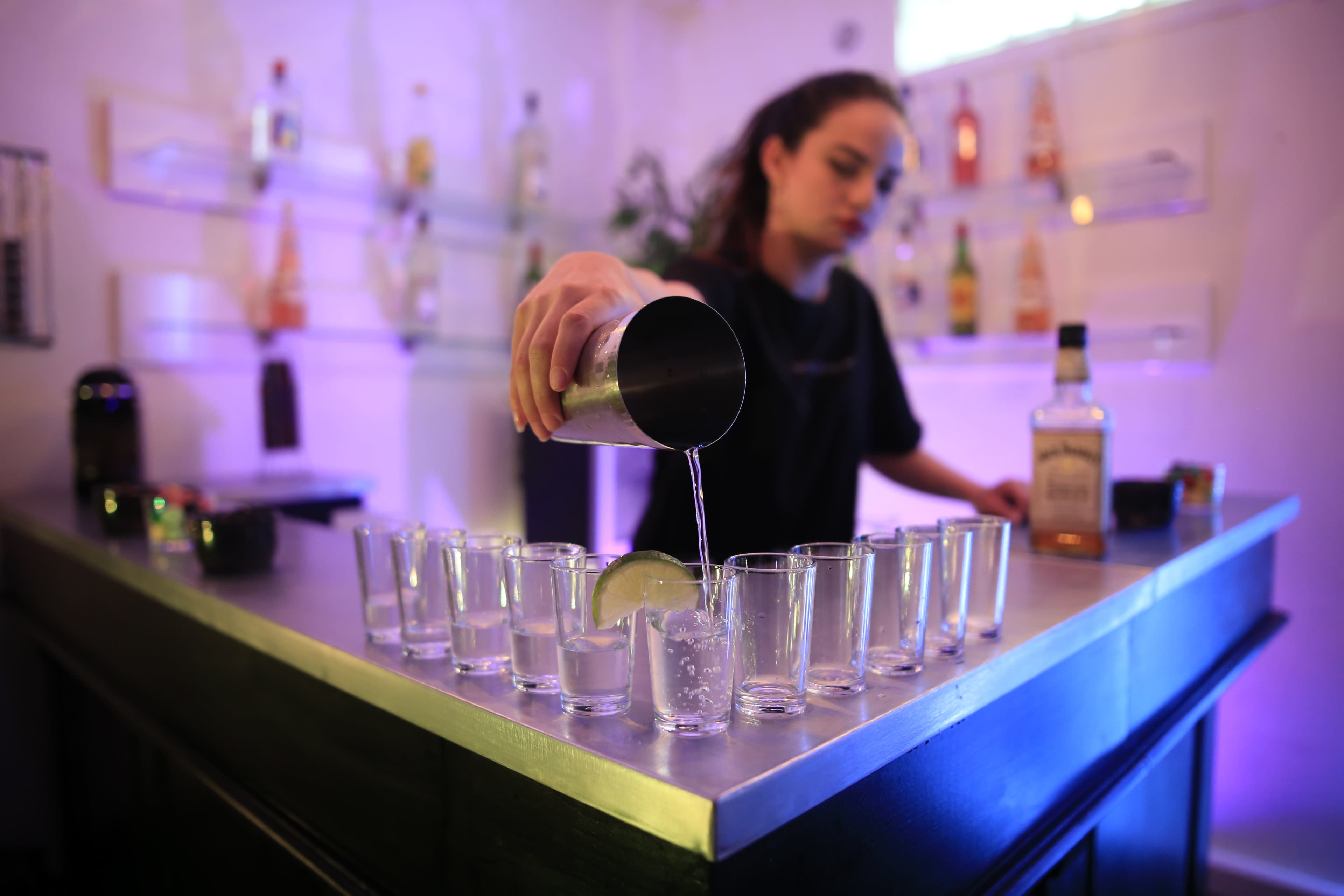A bartender is pouring a drink into a shot glass lined up on a bar counter.