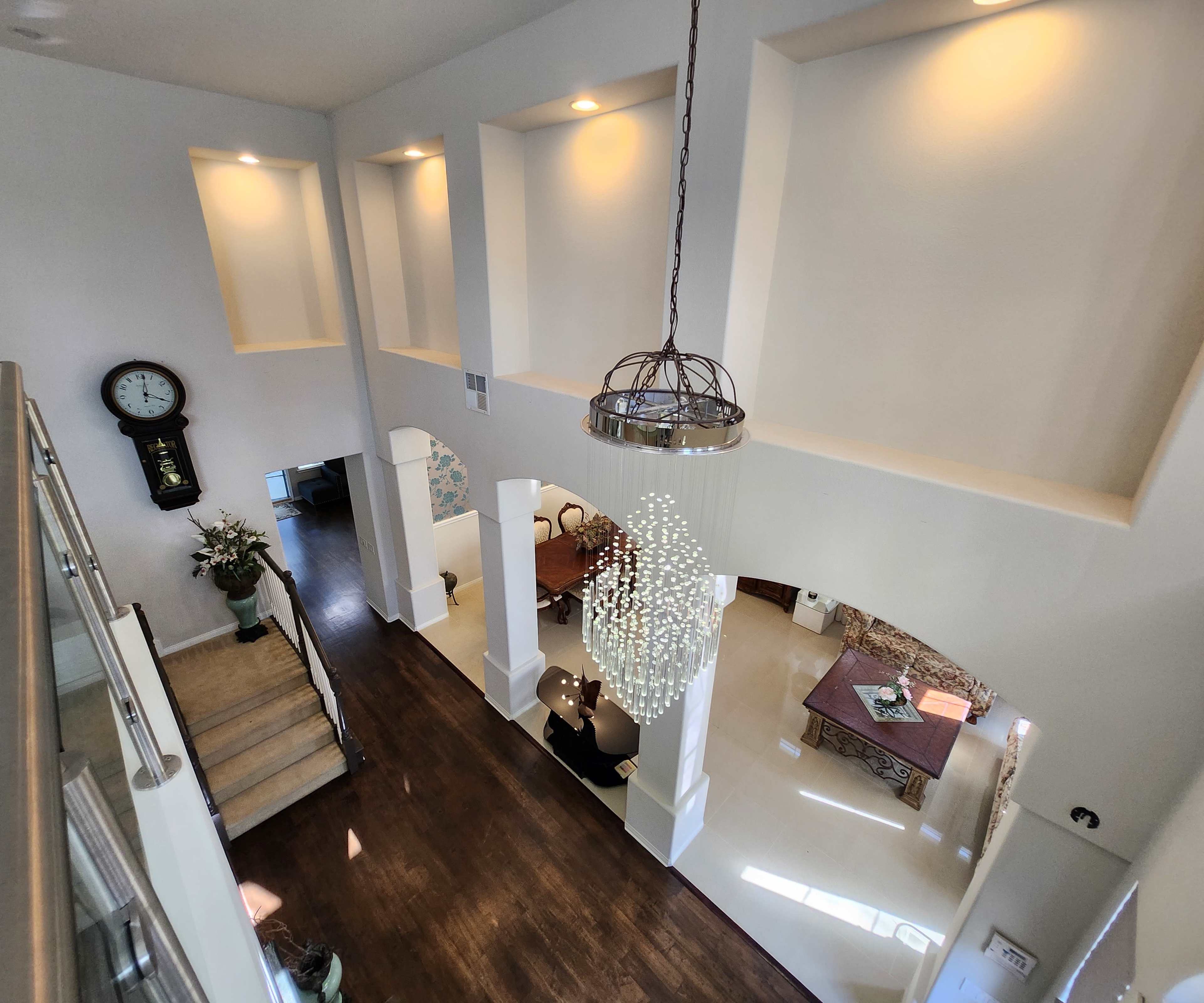 A spacious indoor entryway with a staircase leading up, large windows, and a modern chandelier illuminating the area.