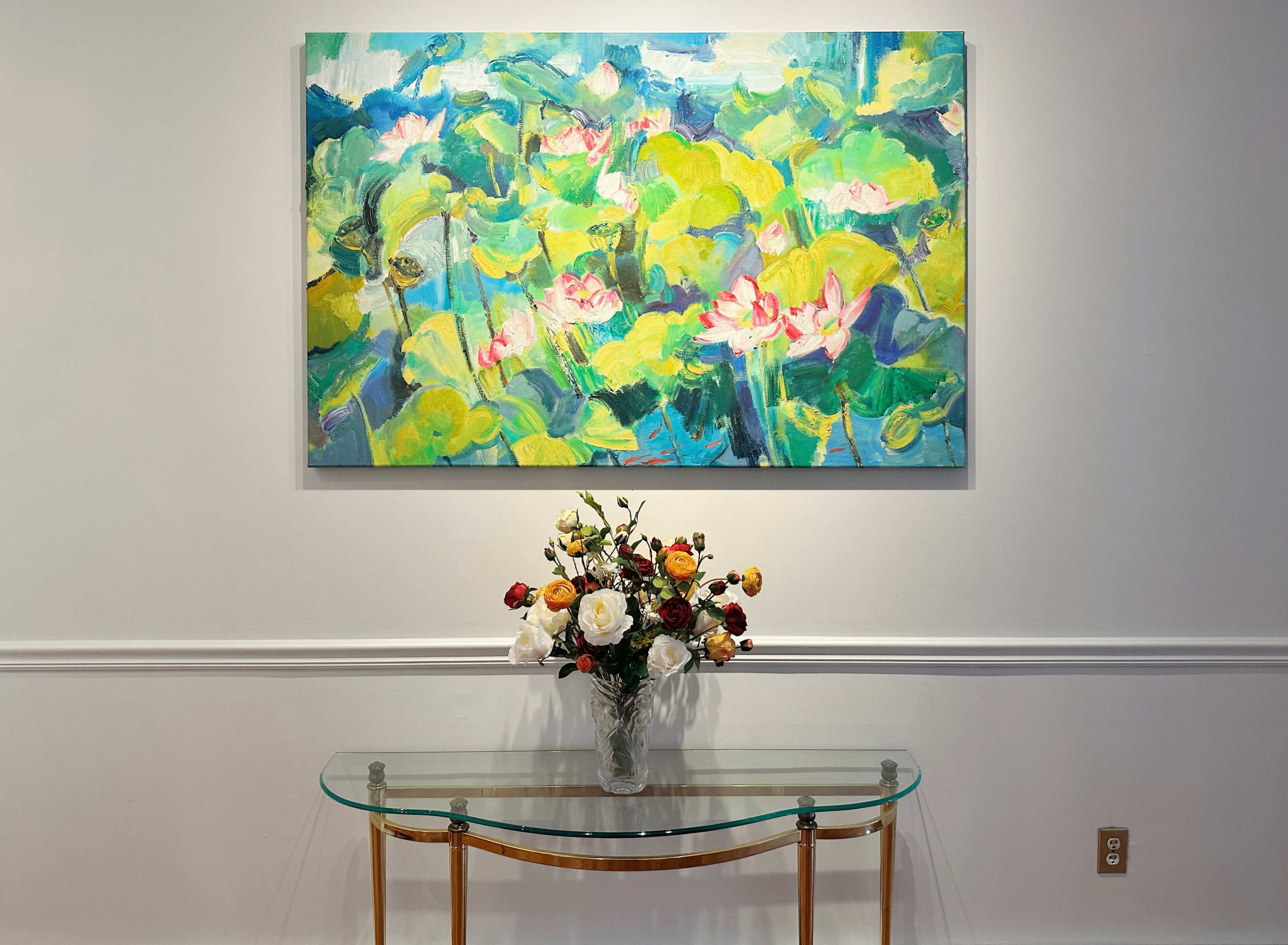 A floral painting hangs above a glass console table adorned with a vase of mixed flowers.