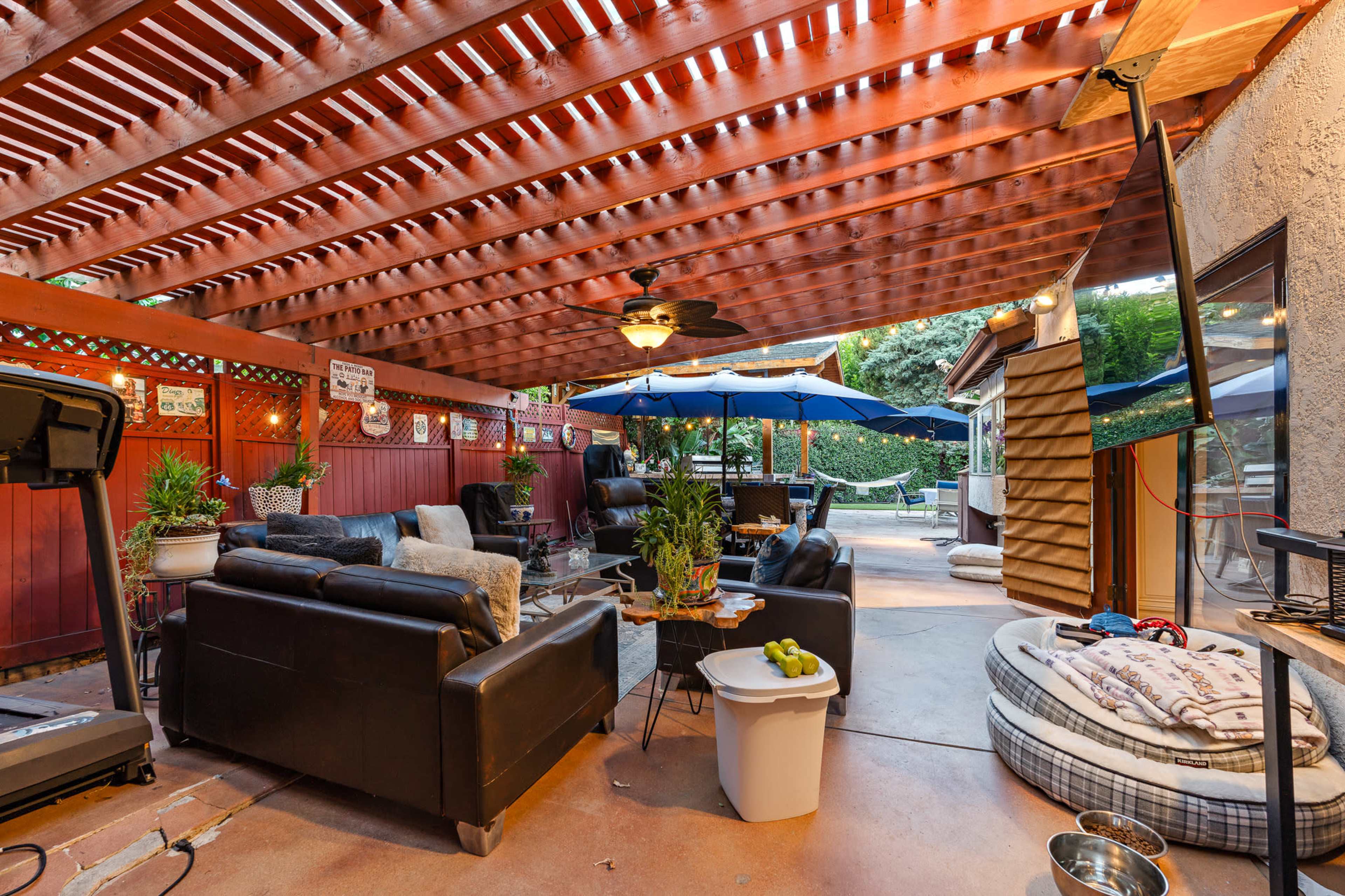 The image shows a covered outdoor patio with black seating, a large umbrella over a table, and a dog bed in the corner.
