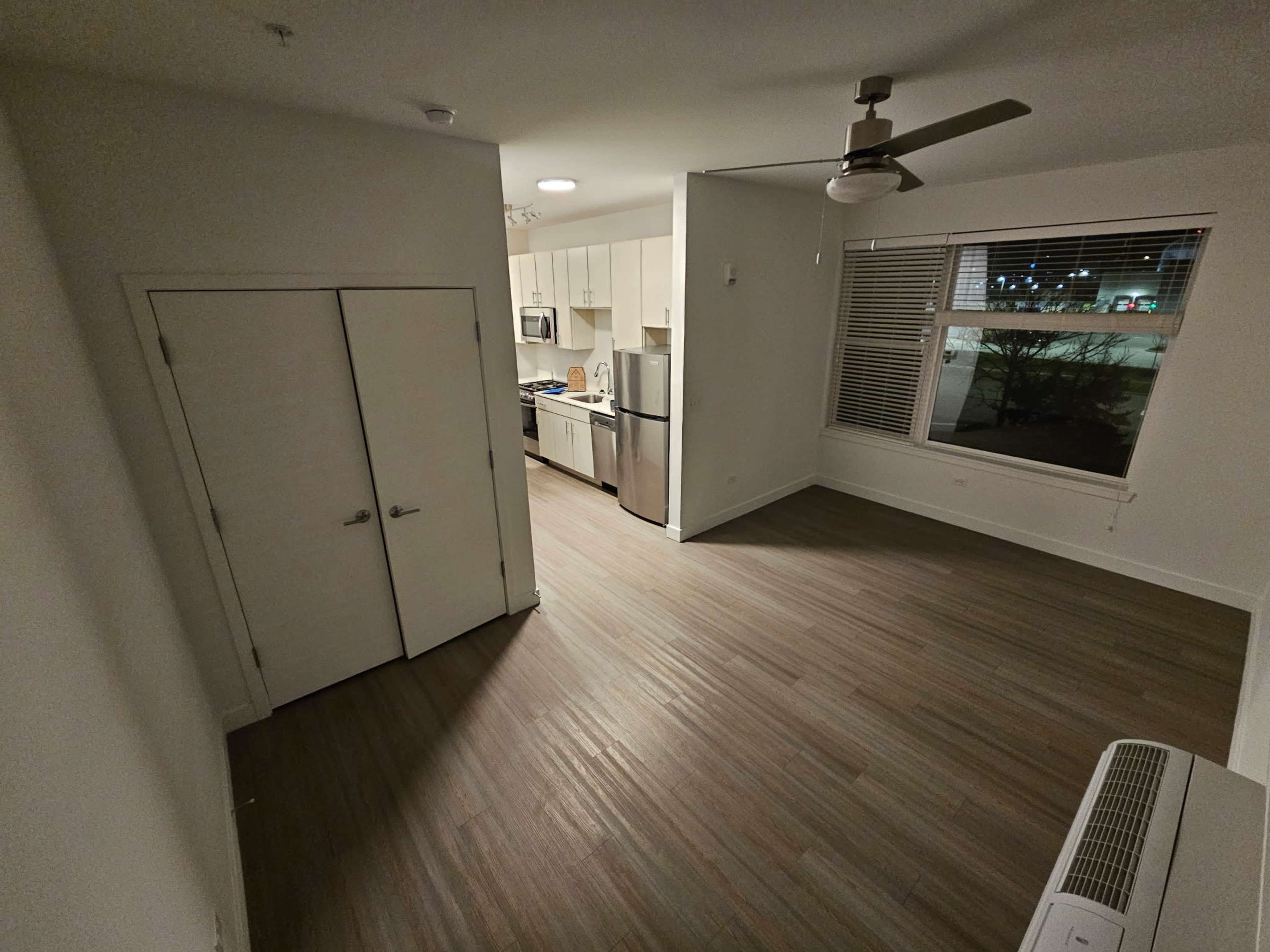 The image shows a well-lit apartment interior featuring a kitchen area with modern appliances and an open living space with wooden flooring.