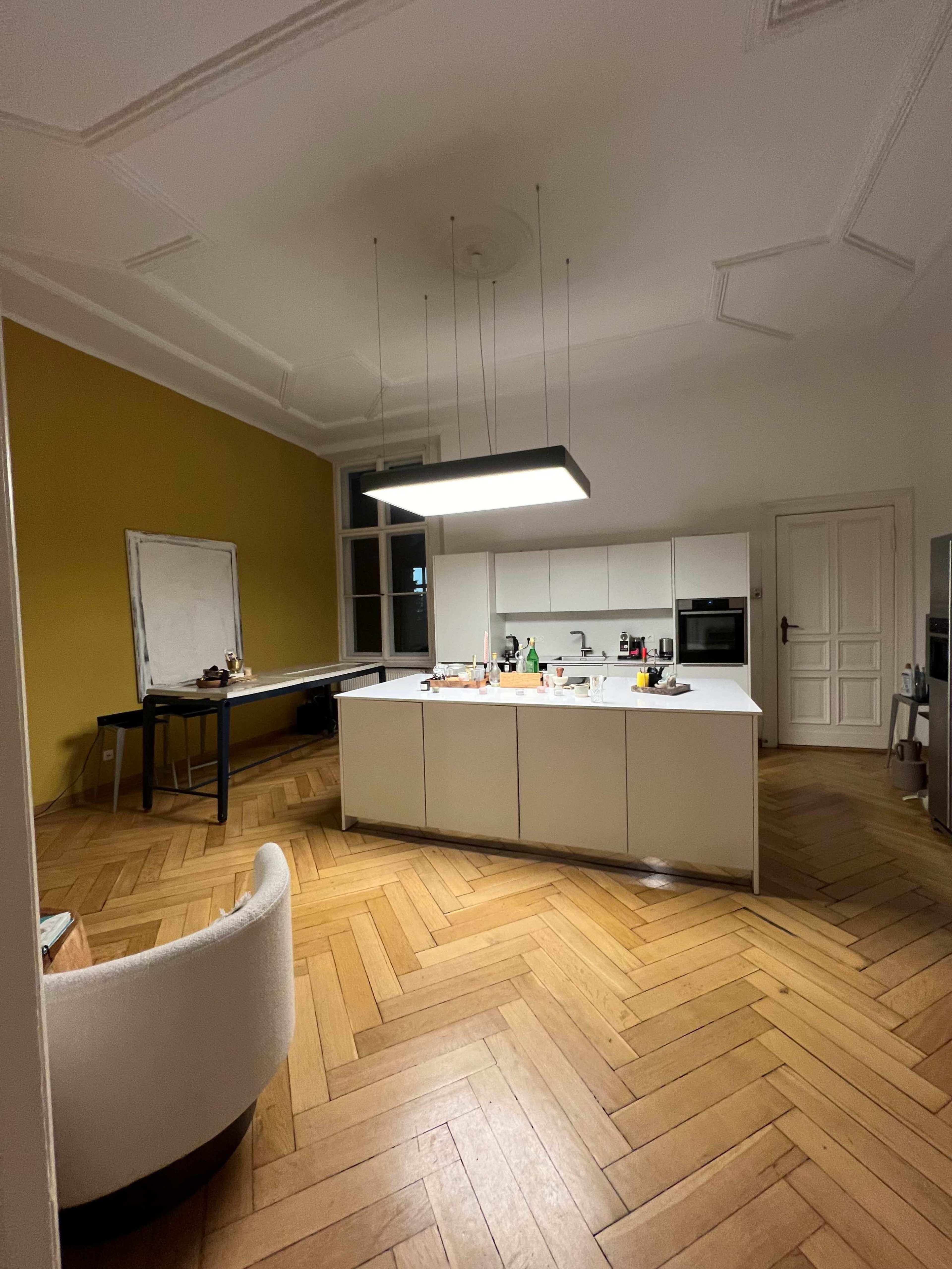 A modern kitchen with a central island, surrounded by wooden flooring and featuring a yellow accent wall.