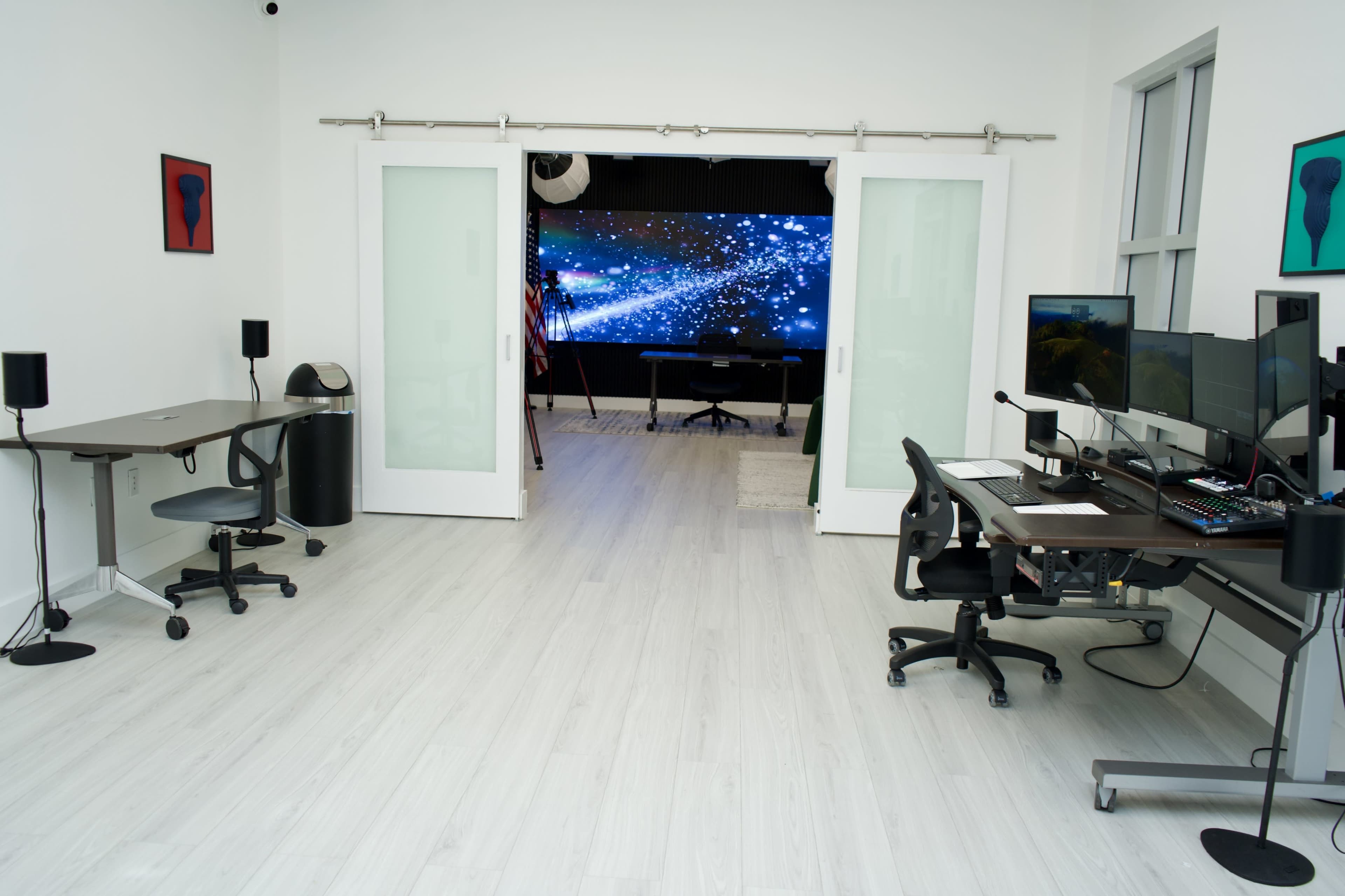 The image shows a modern office space with two desks on the sides and a large screen displaying a starry scene in the background.