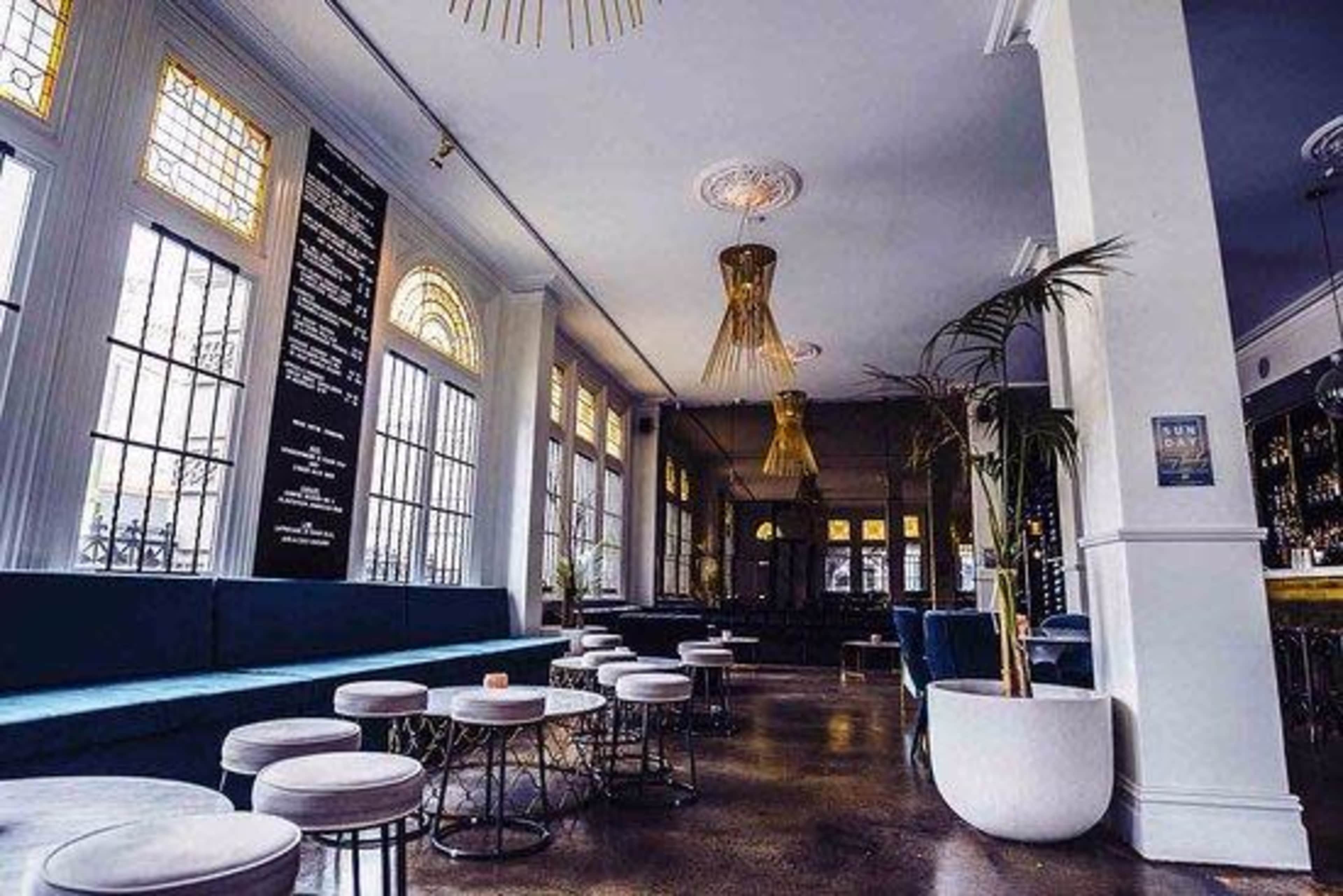 A modern café interior with a long blue bench, round tables, and elegant lighting fixtures.