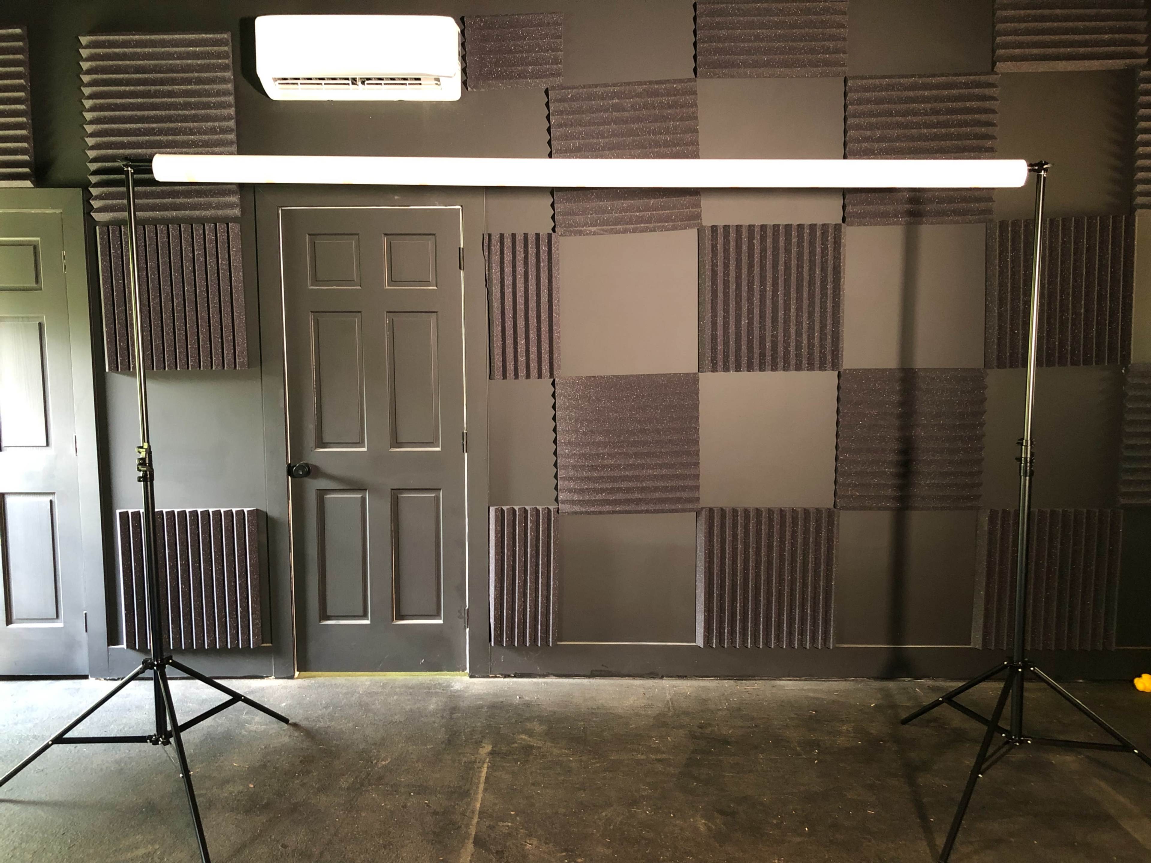 A photography setup with a lightbar mounted on stands in a room featuring a black wall with sound-absorbing panels and a closed door.